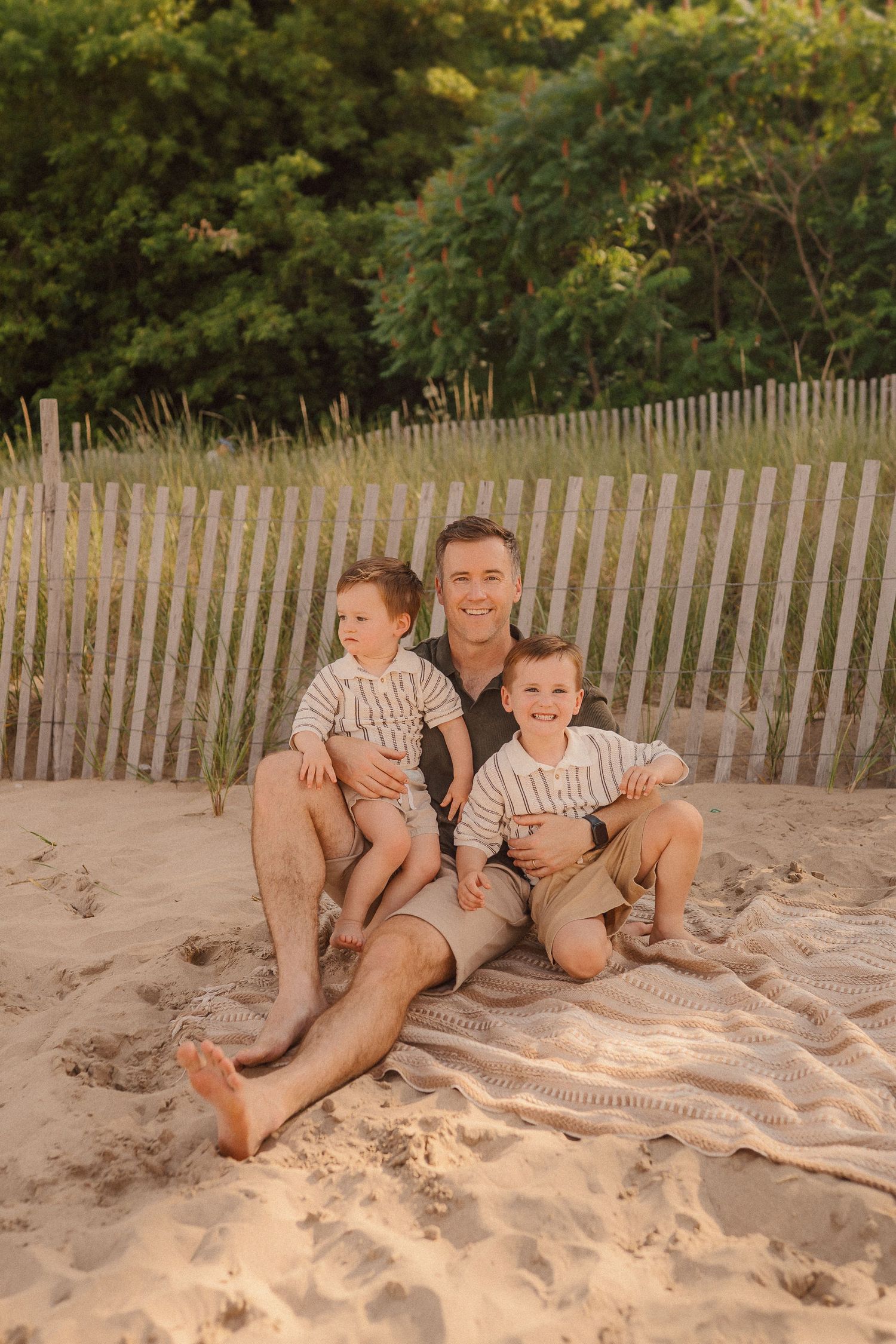 People relaxing and playing together on a sandy beach with a wooden fence visible in the background.