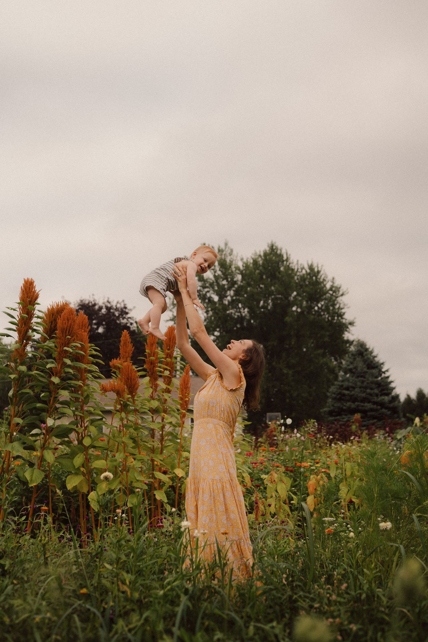 A person in a yellow dress dances joyfully among tall flowering plants in a garden at dusk.