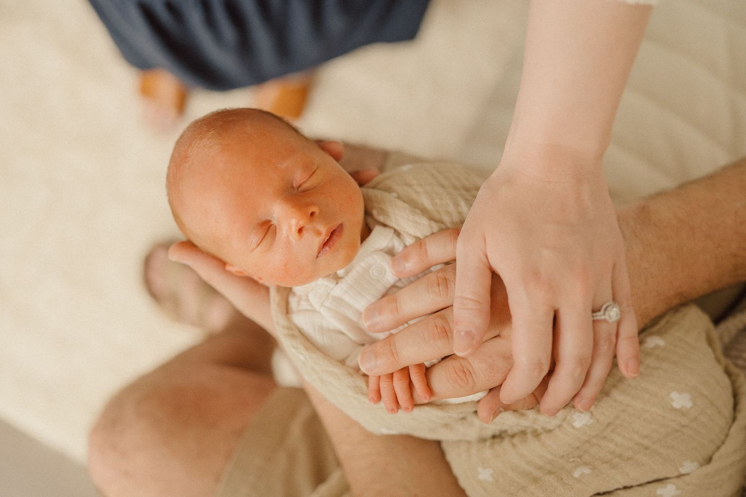 Close-up photo of sleeping newborn baby being gently held in parents' hands.