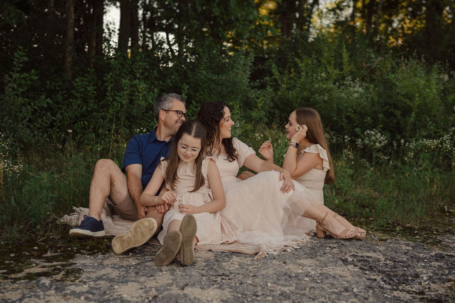 Family relaxes together on natural stone formations during an outdoor photo session at dusk.
