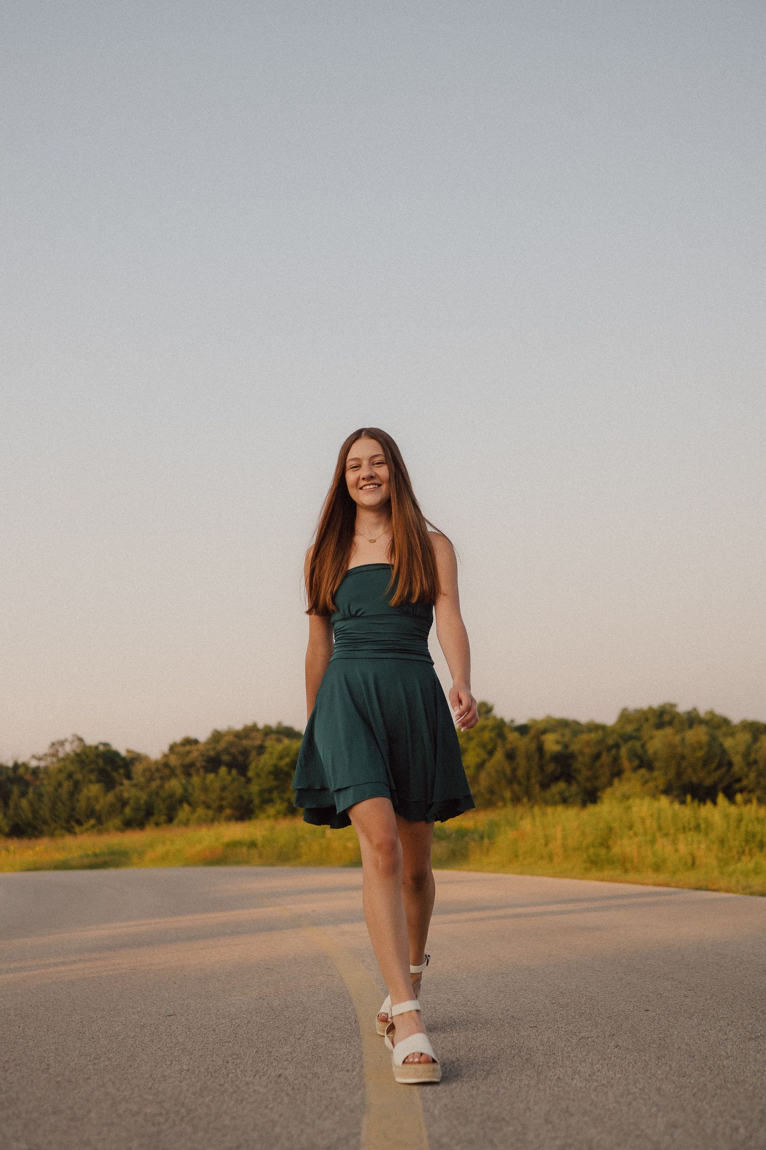 A woman in a green dress walks gracefully down an empty country road at golden hour.