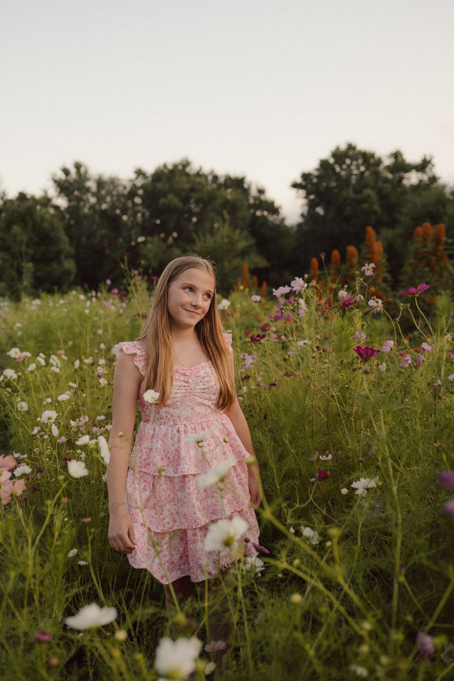 A pink floral dress stands out among wild cosmos and zinnia flowers in a summer garden.