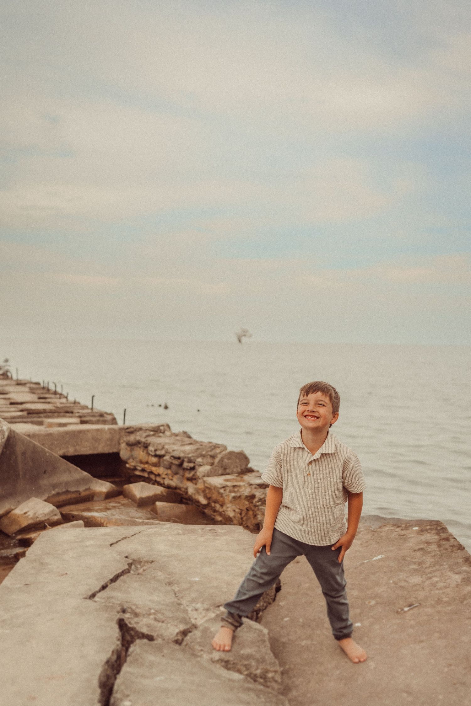 A joyful scene on a rocky beach as someone explores the shoreline in casual summer attire.