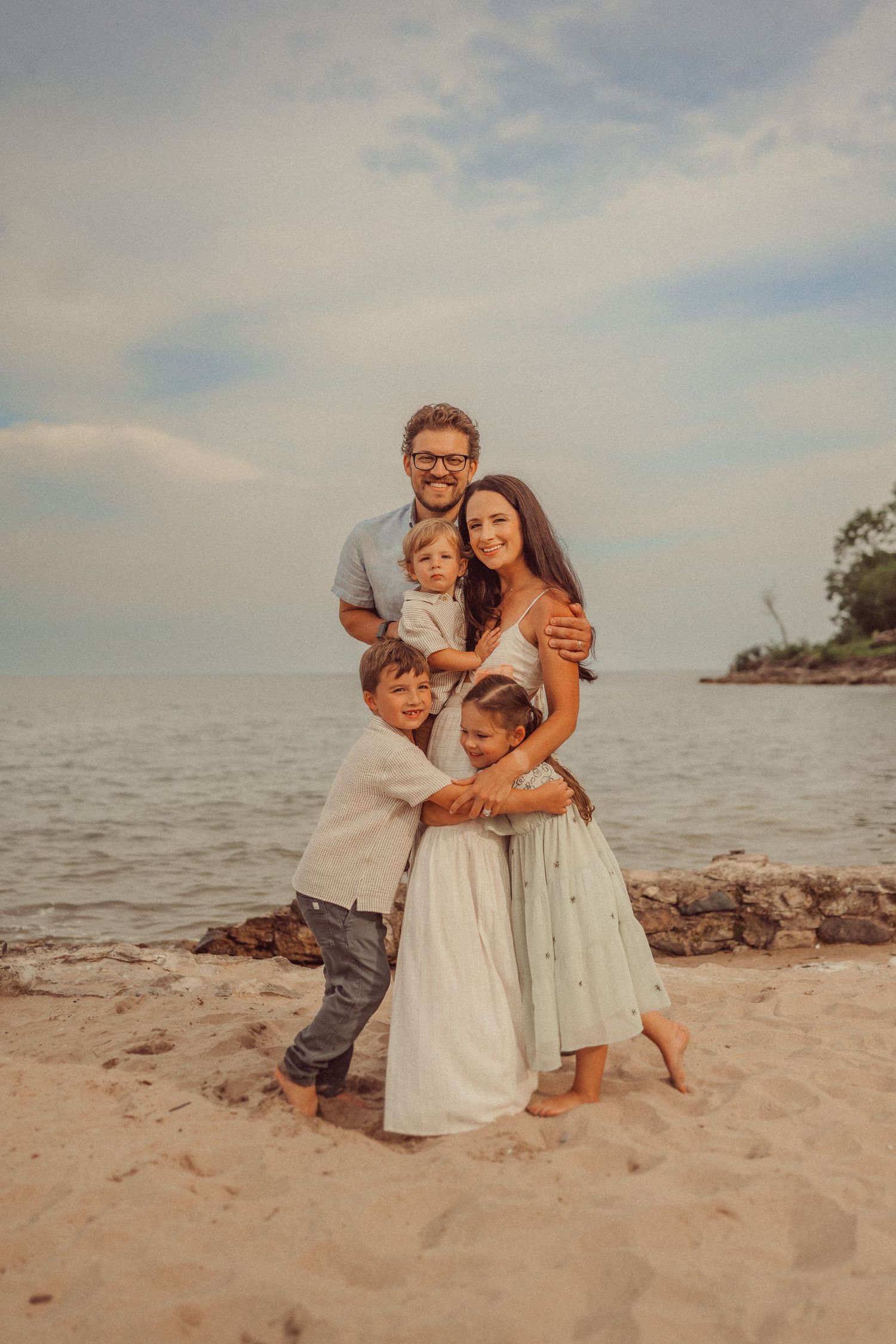 A family embraces in matching outfits during a beach photo session at sunset.