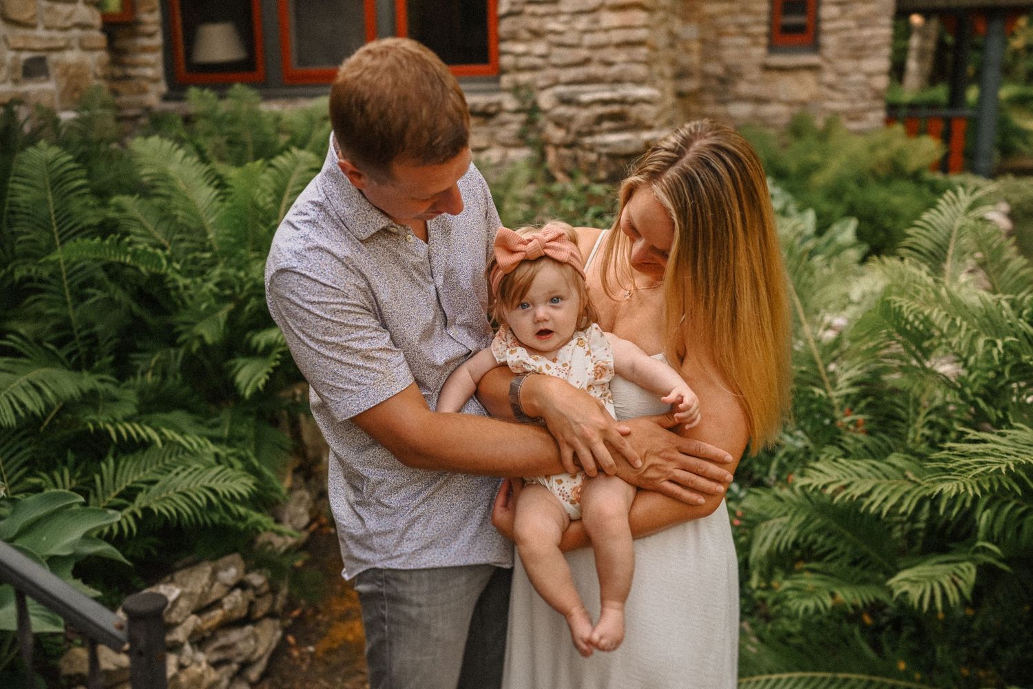An intimate family portrait amidst lush ferns outside a stone cottage.