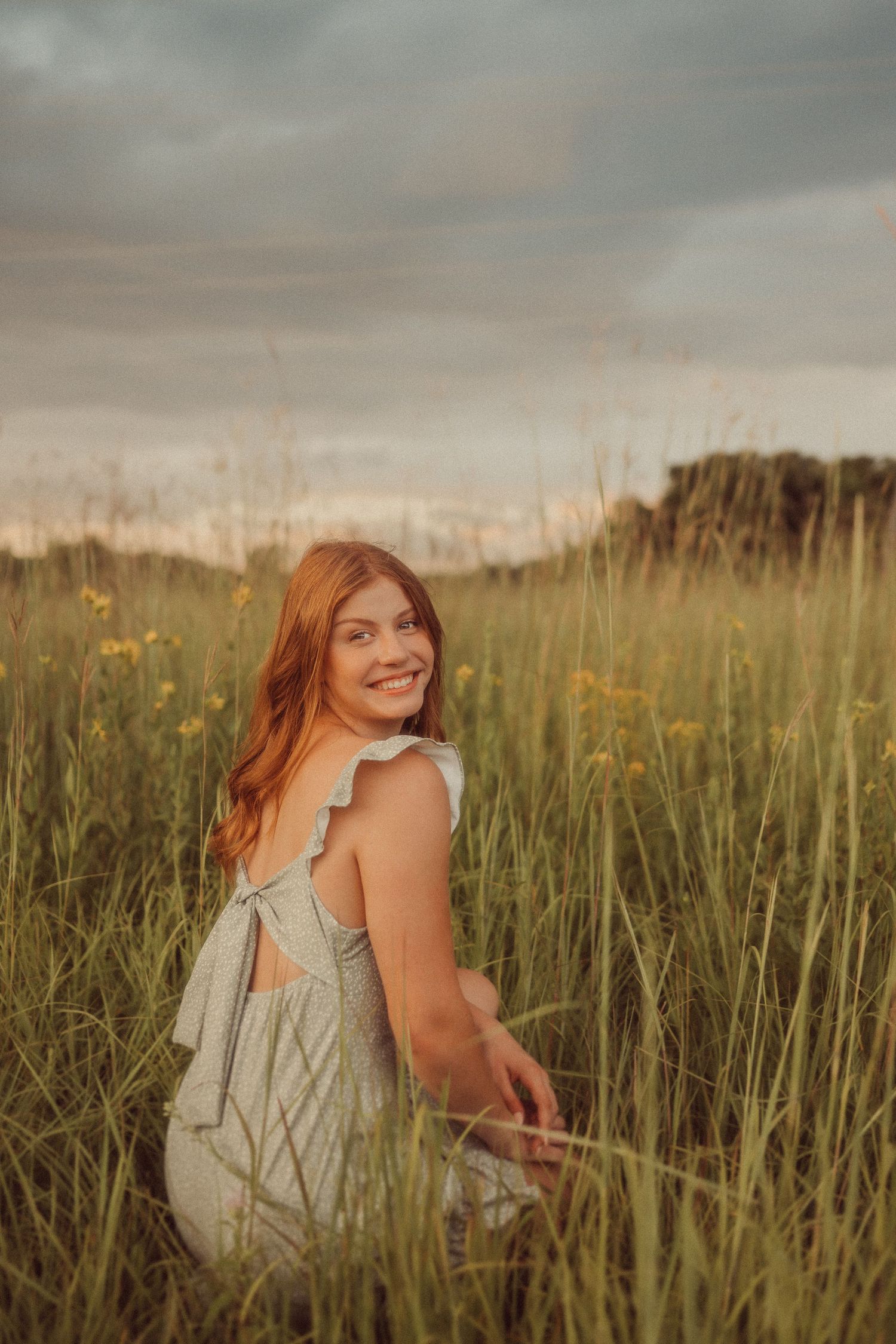 Dreamy sunset portrait in a wild meadow with tall grass and wildflowers.