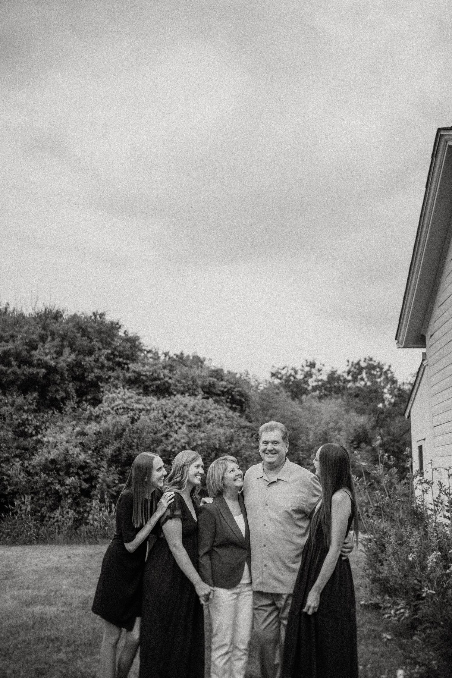 Black and white photograph of a group gathered beside a white house with trees in background.