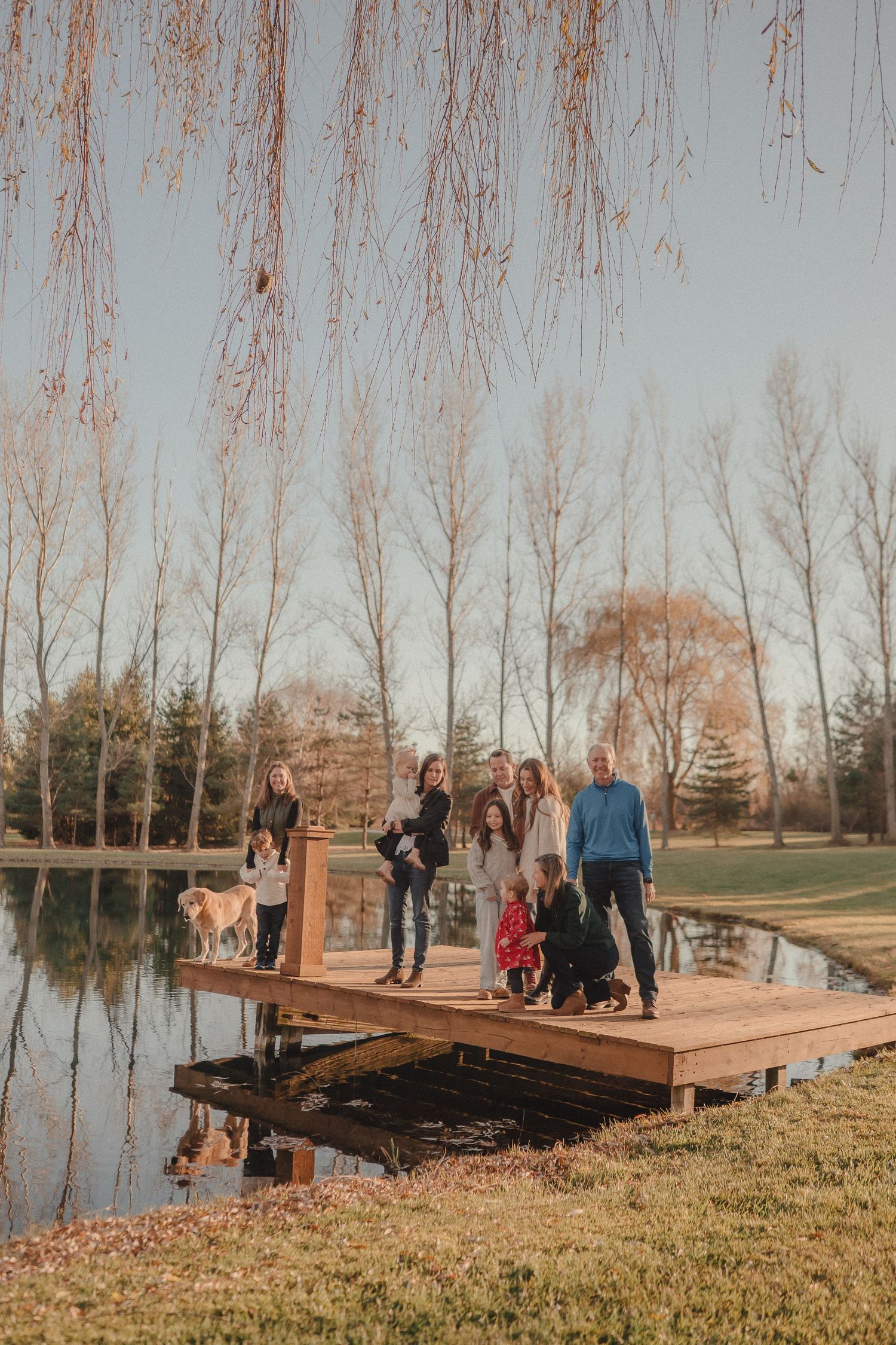 Group gathered on wooden deck overlooking pond during autumn sunset.