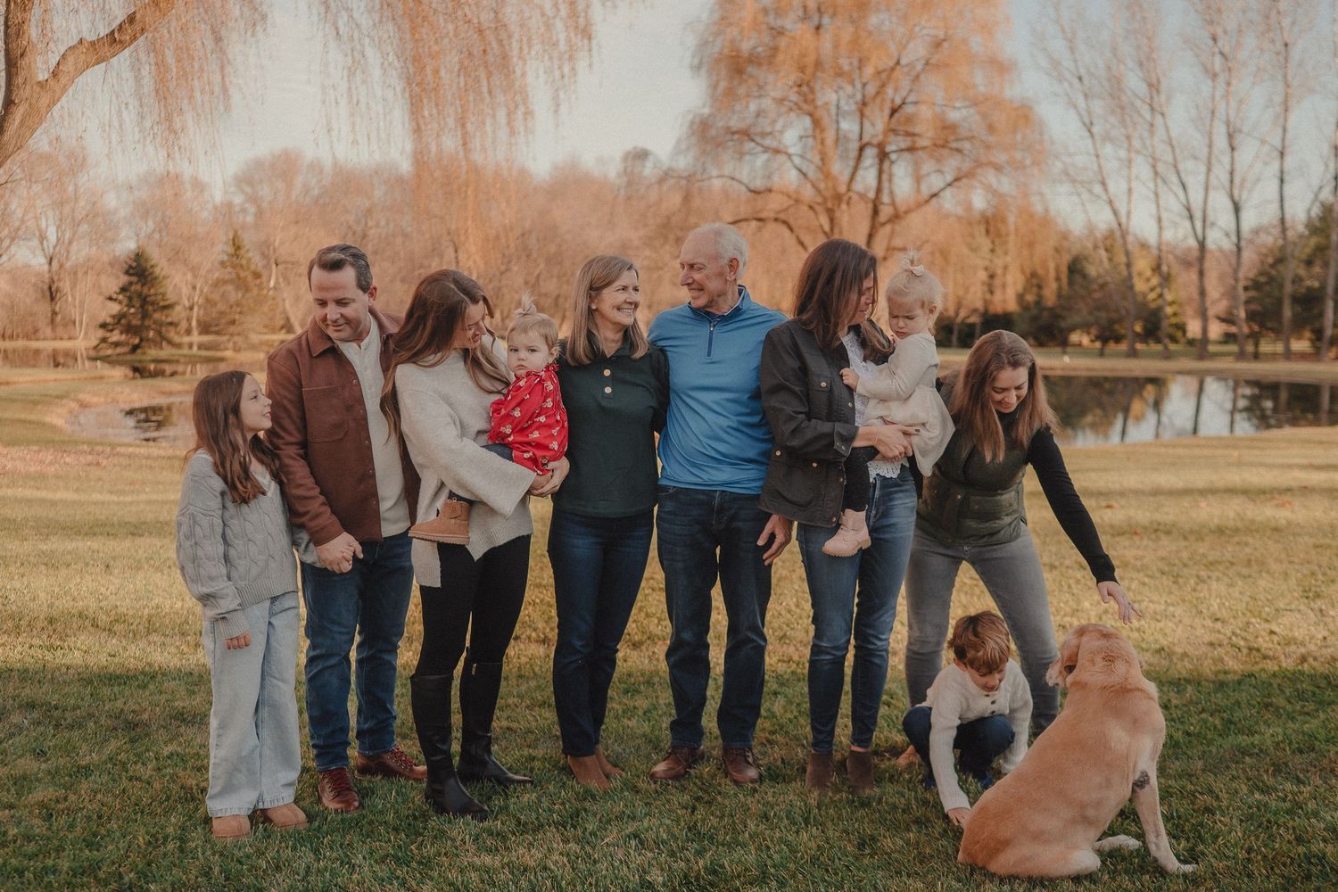 Multiple people standing together in a grassy field with autumn trees creating a warm backdrop.
