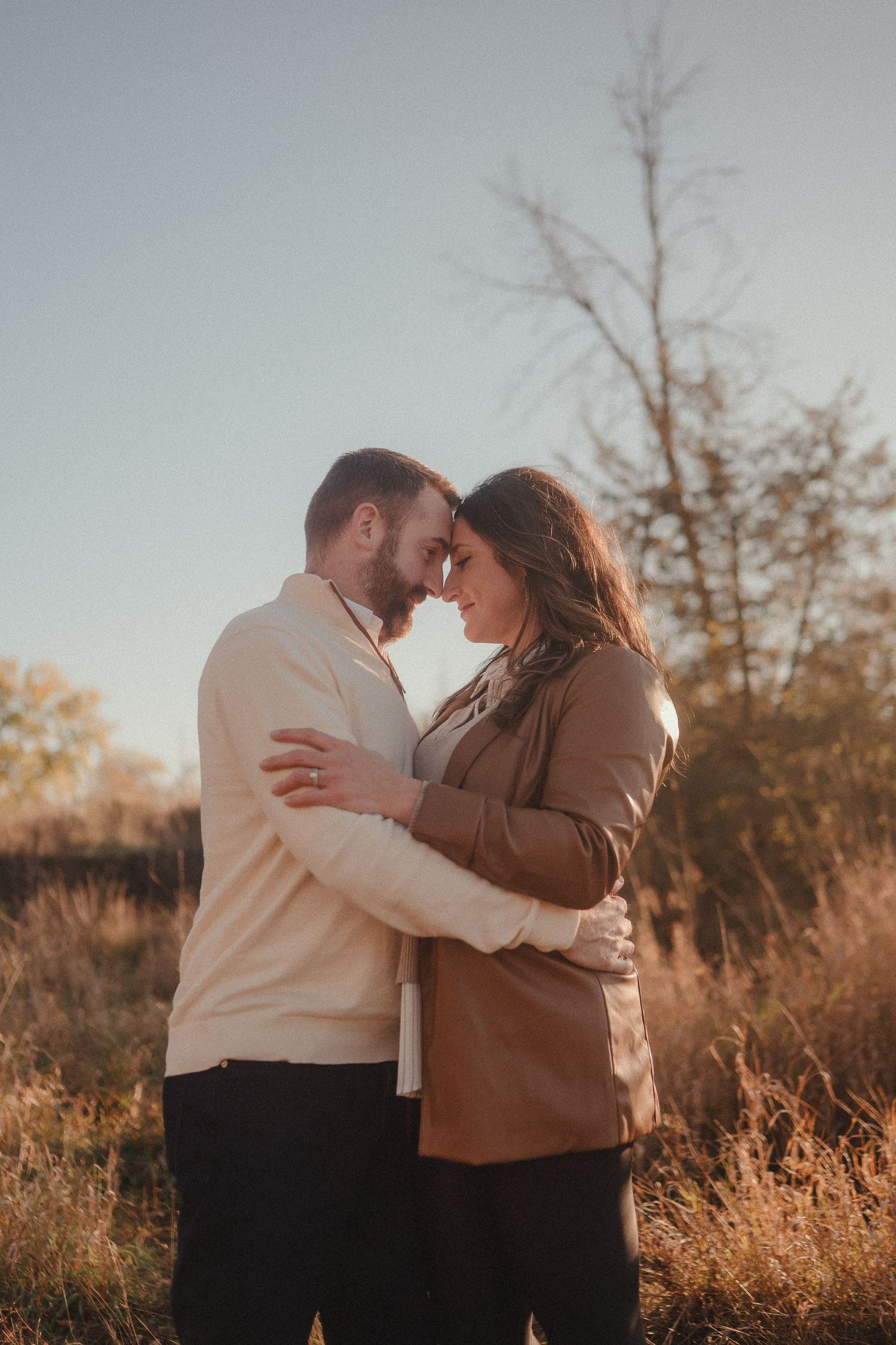 A couple shares an intimate moment in autumn field wearing neutral colored sweaters.