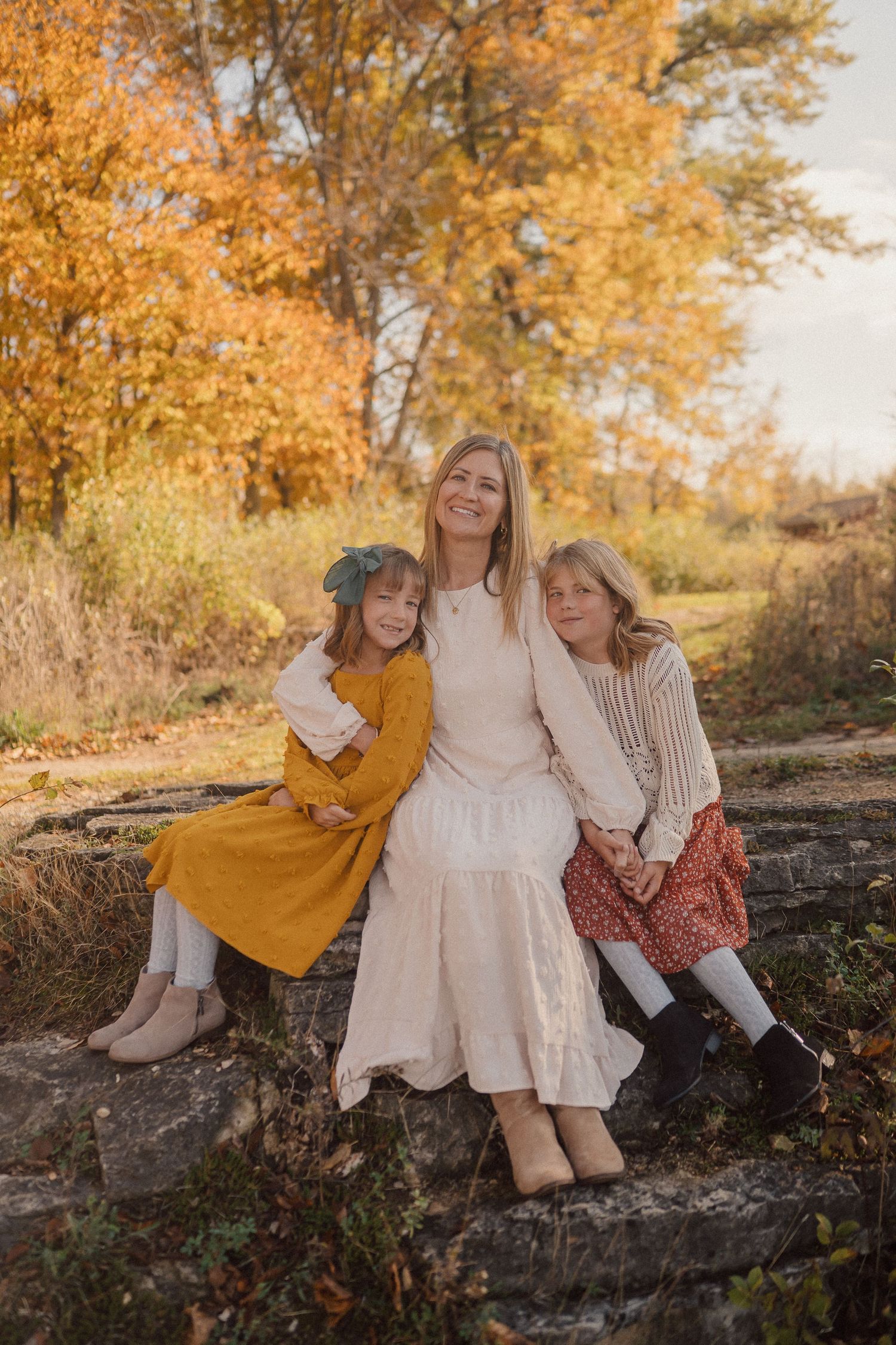 Casual outdoor portrait of three people sitting on a stone wall during golden hour.