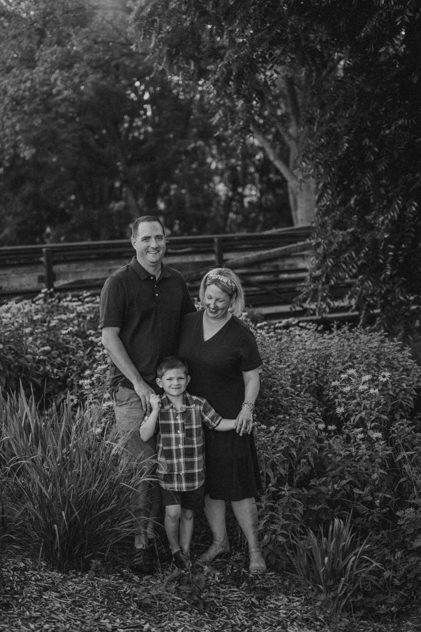Black and white family portrait in garden setting with rustic fence background.