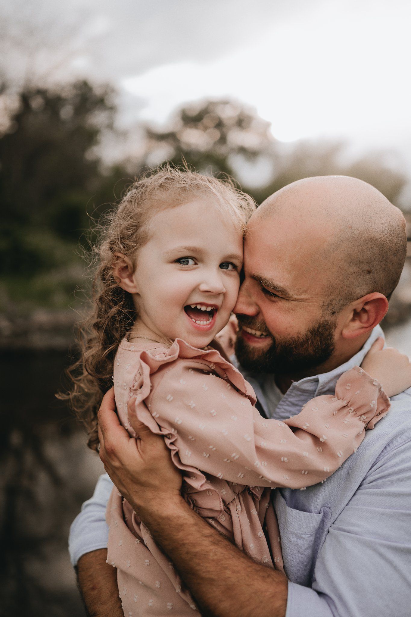 A tender candid moment between a parent and child laughing together outdoors.