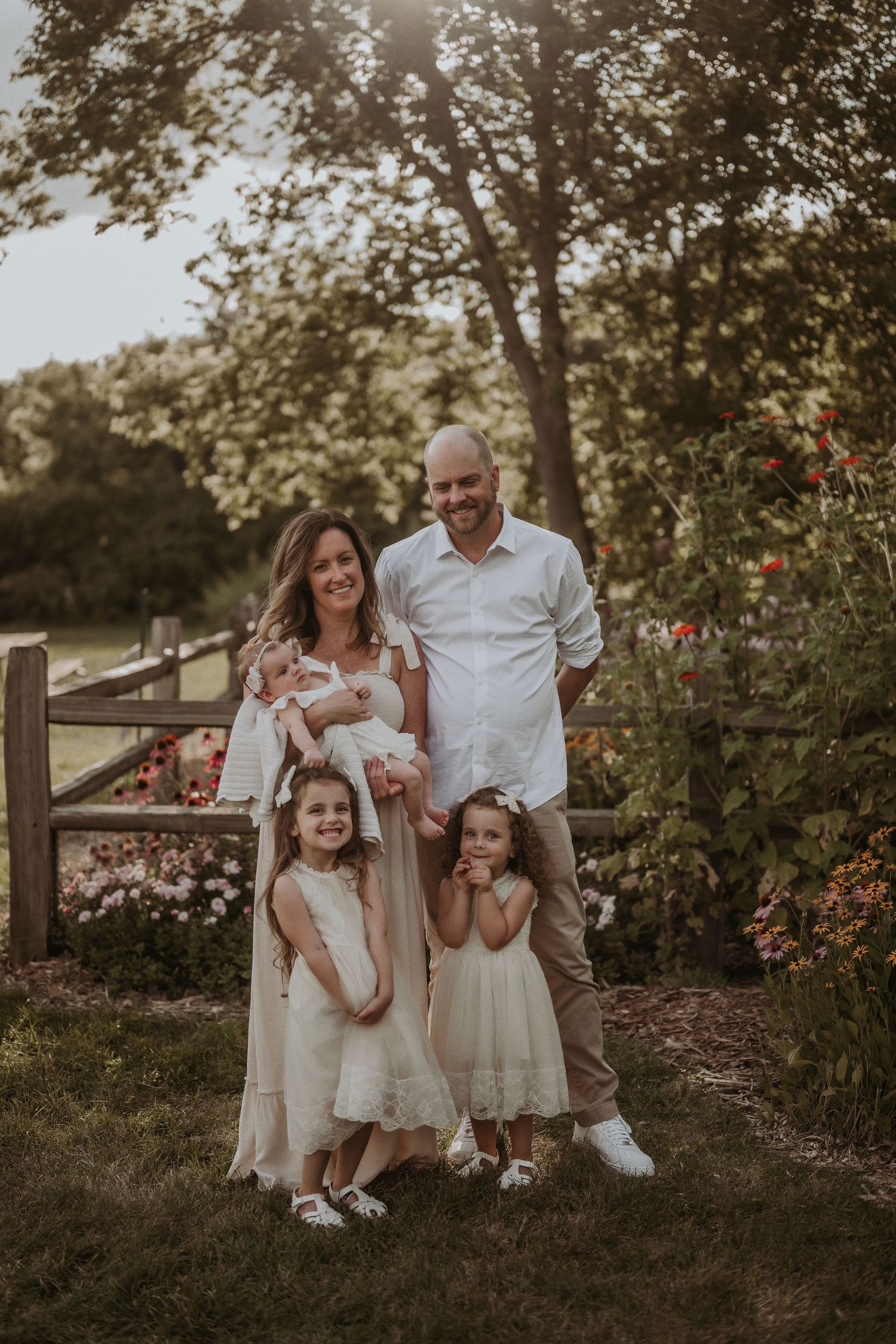 Family of four in coordinated white and cream outfits pose together in a sunset garden setting.
