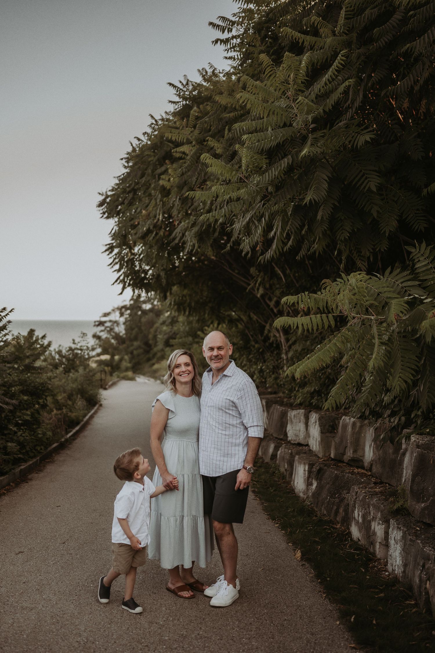A casual family portrait on a winding path surrounded by lush ferns and stone walls.