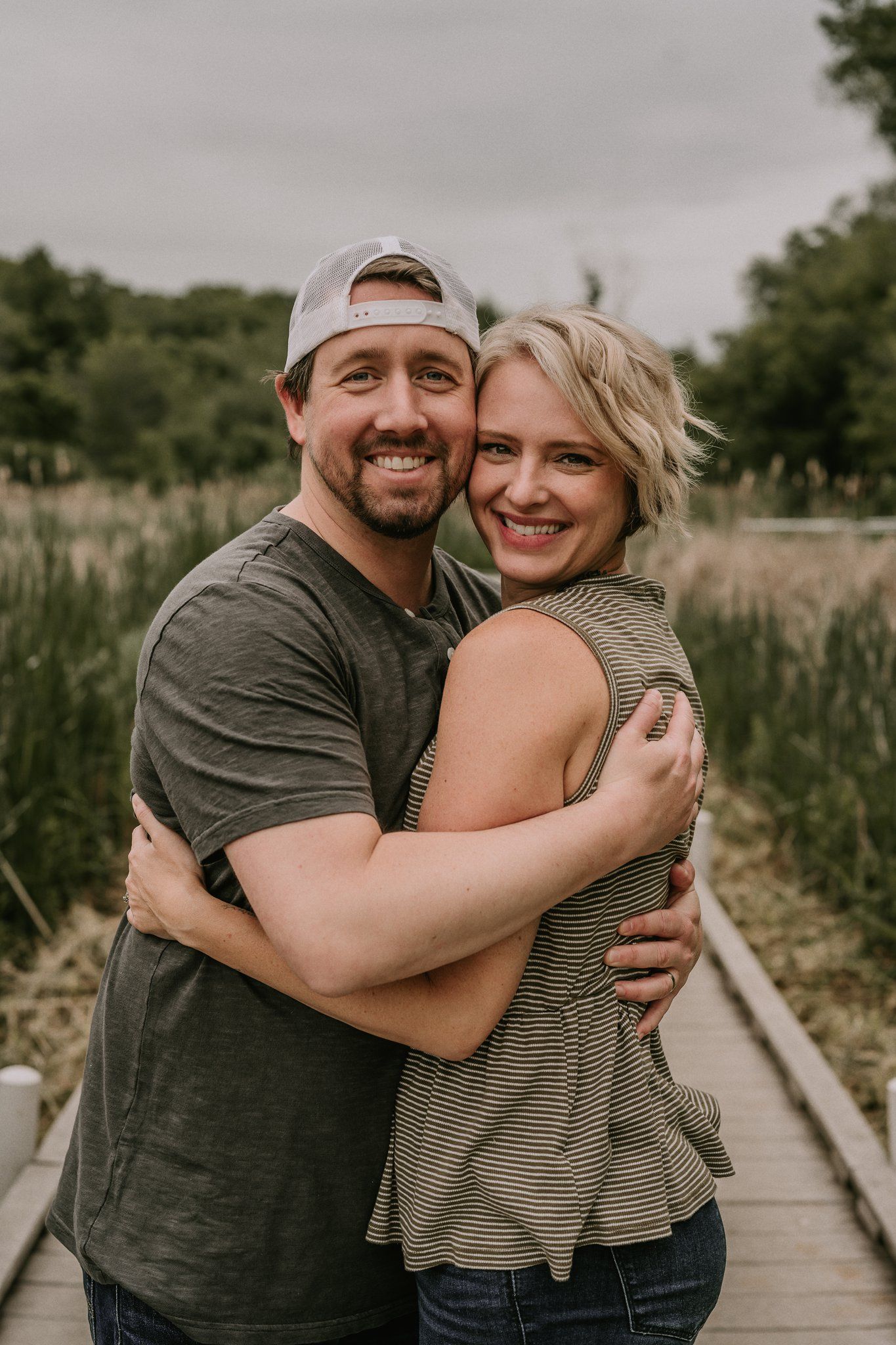 Couple embracing and smiling on a wooden boardwalk surrounded by natural scenery.