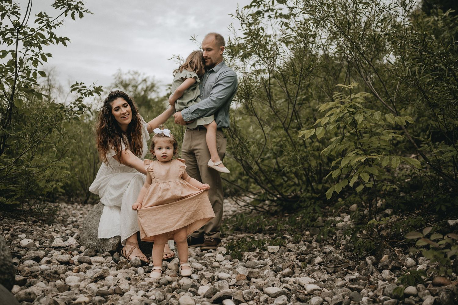 A playful family photo session captured on rocky terrain surrounded by green foliage.