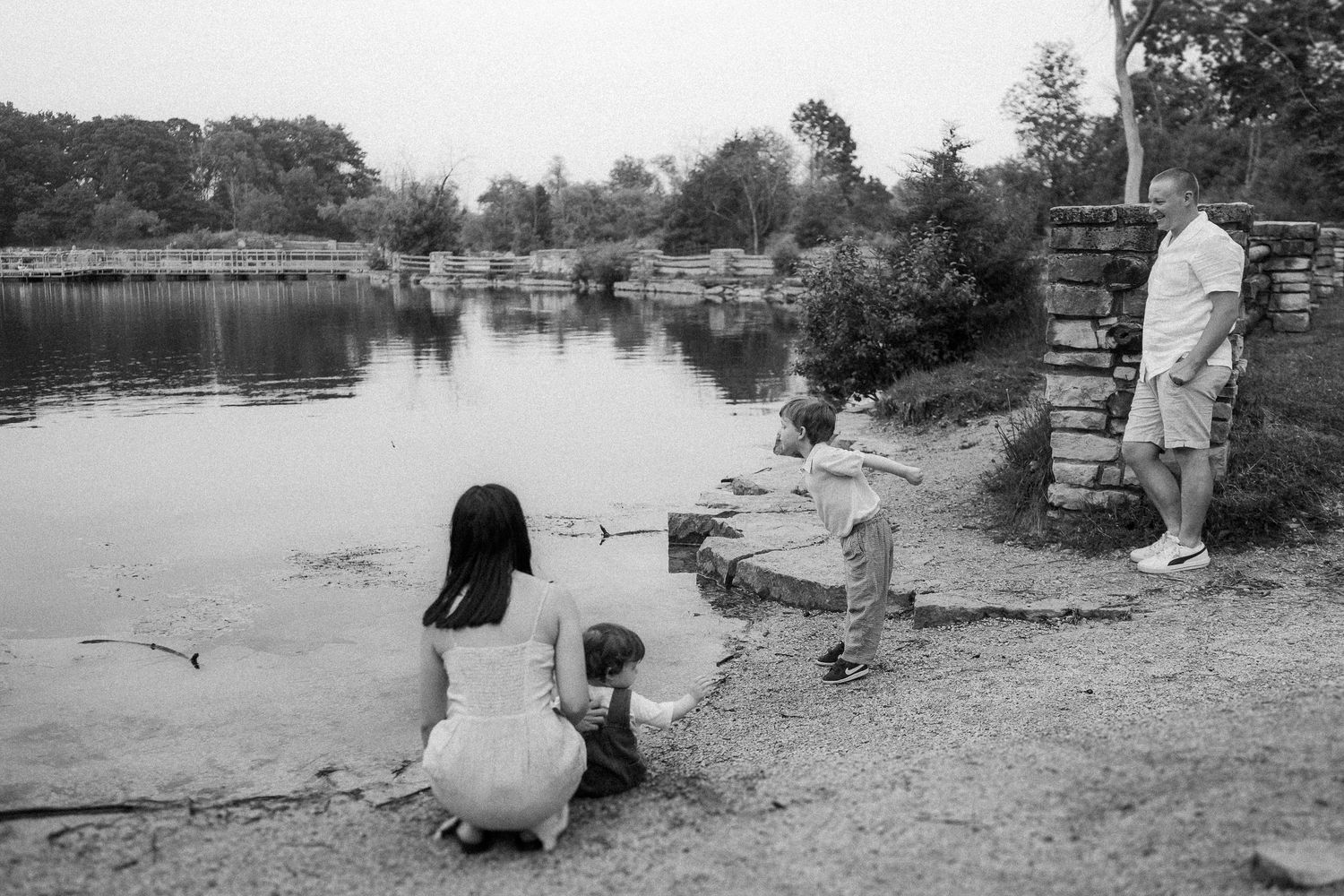 A black and white scene of people sitting by a serene lake with stone walls.