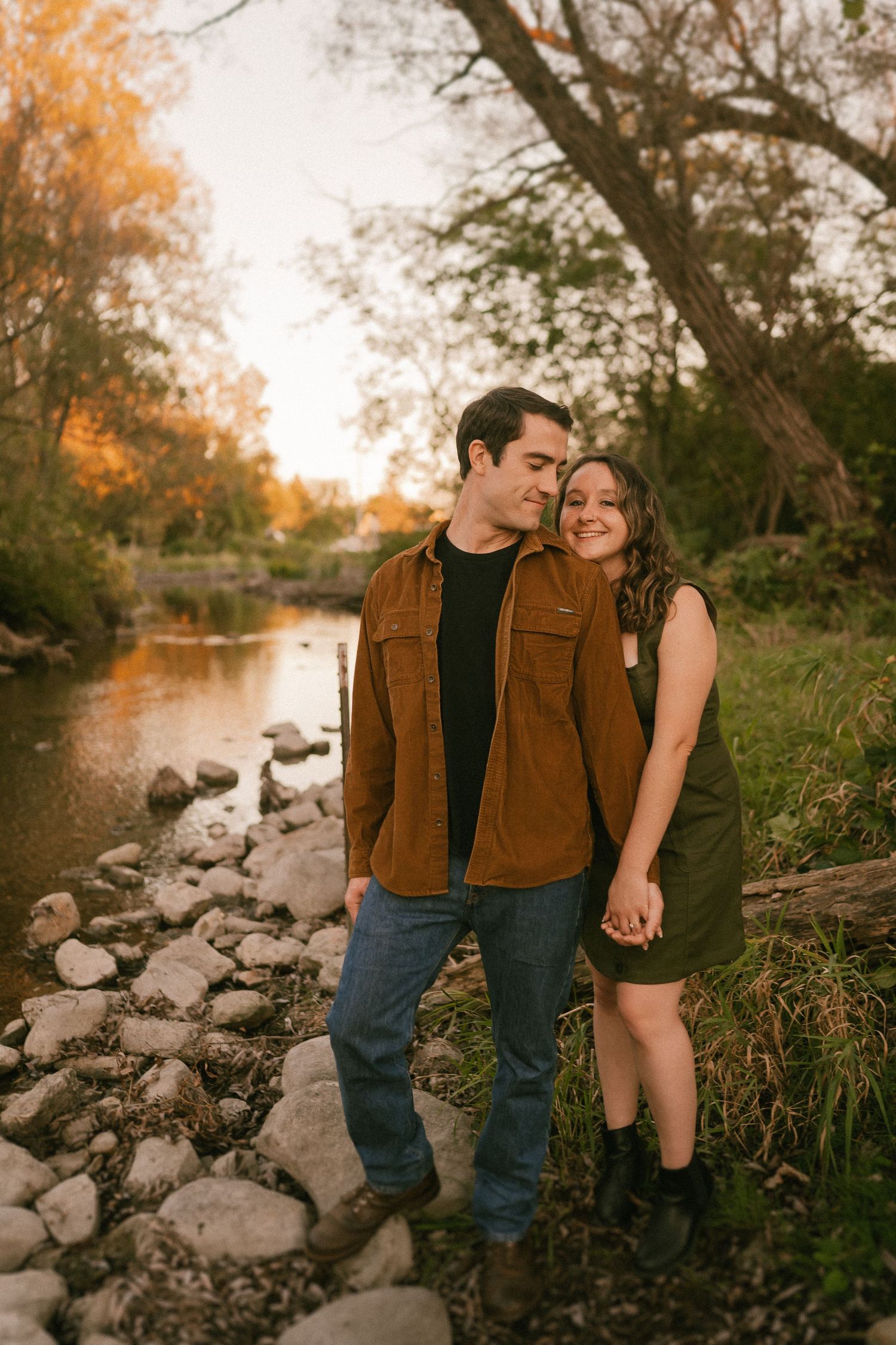 A couple shares a romantic moment by a rocky stream during autumn sunset.