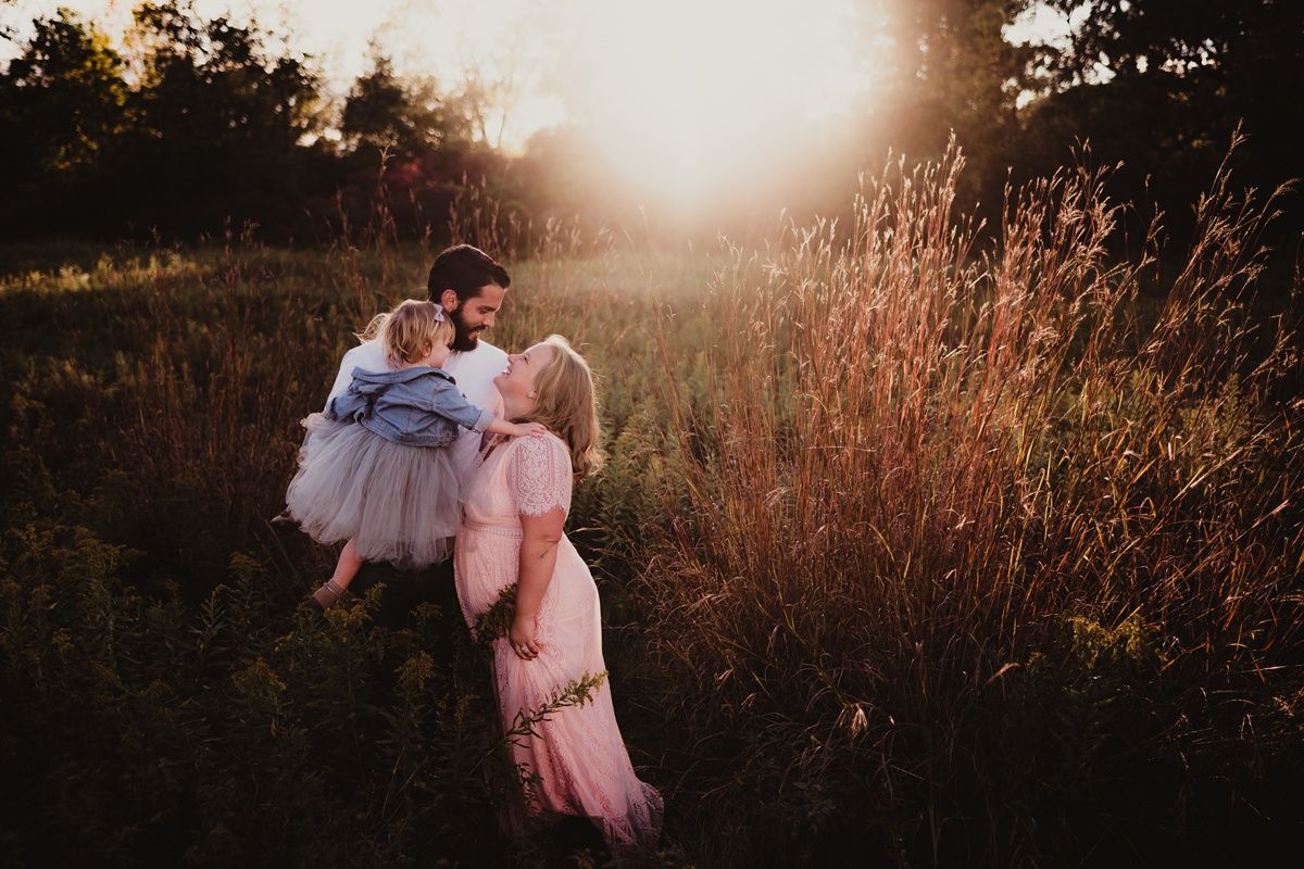 Romantic sunset portrait in a field showing a tender embrace among wildflowers and tall grass.
