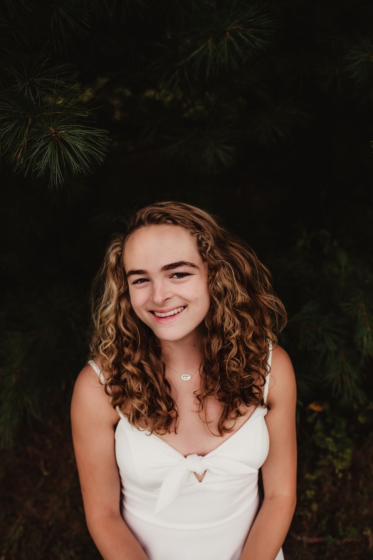 Close-up portrait showing curly hair and joyful expression against dark foliage.