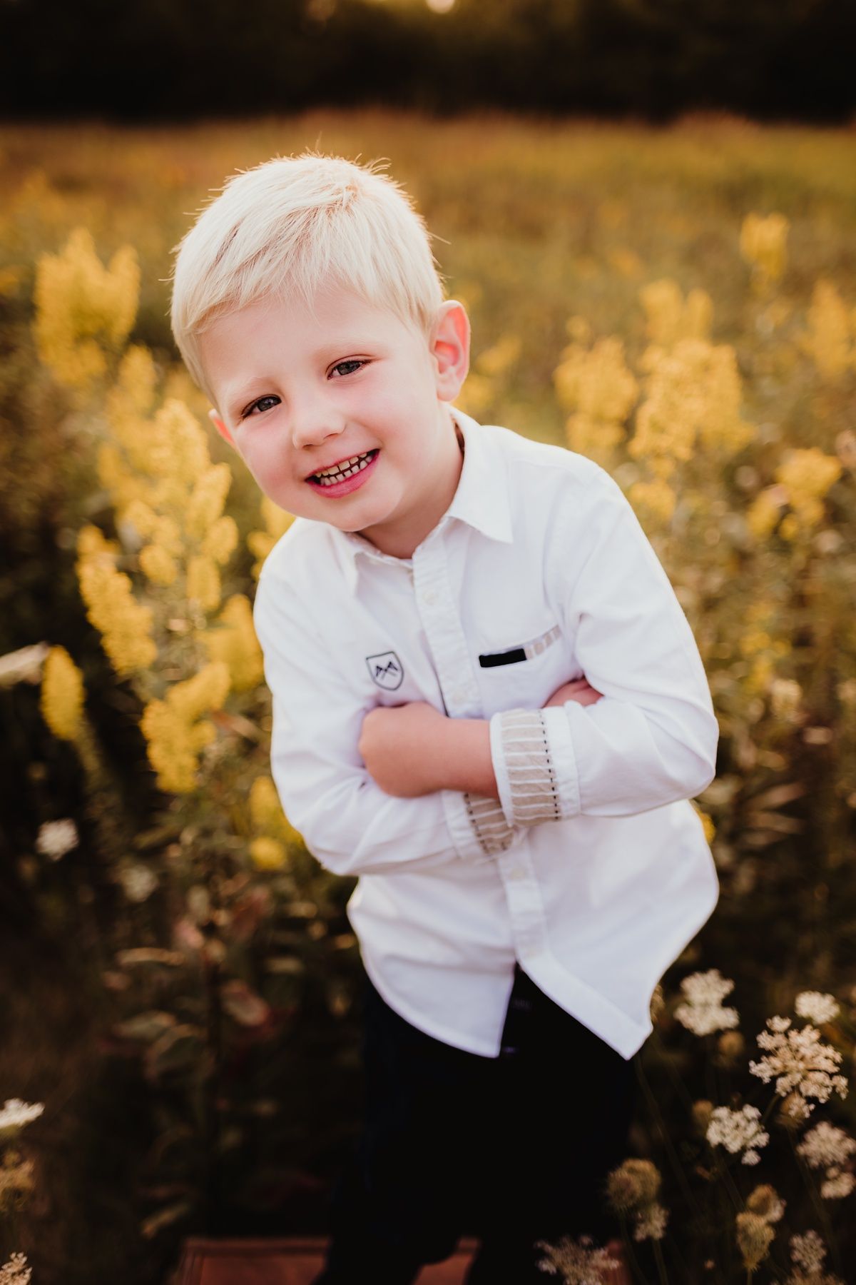 Child in white shirt grins while standing in golden autumn field.
