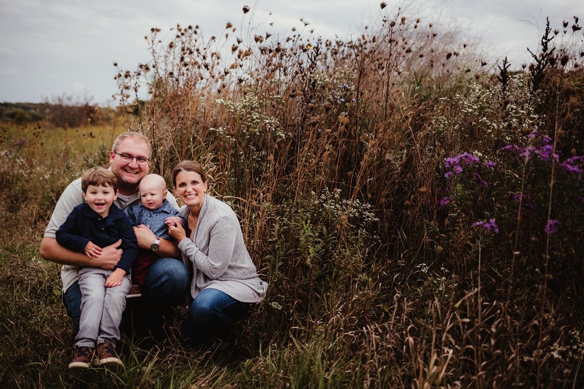 Family poses together among tall wildflowers during autumn sunset.