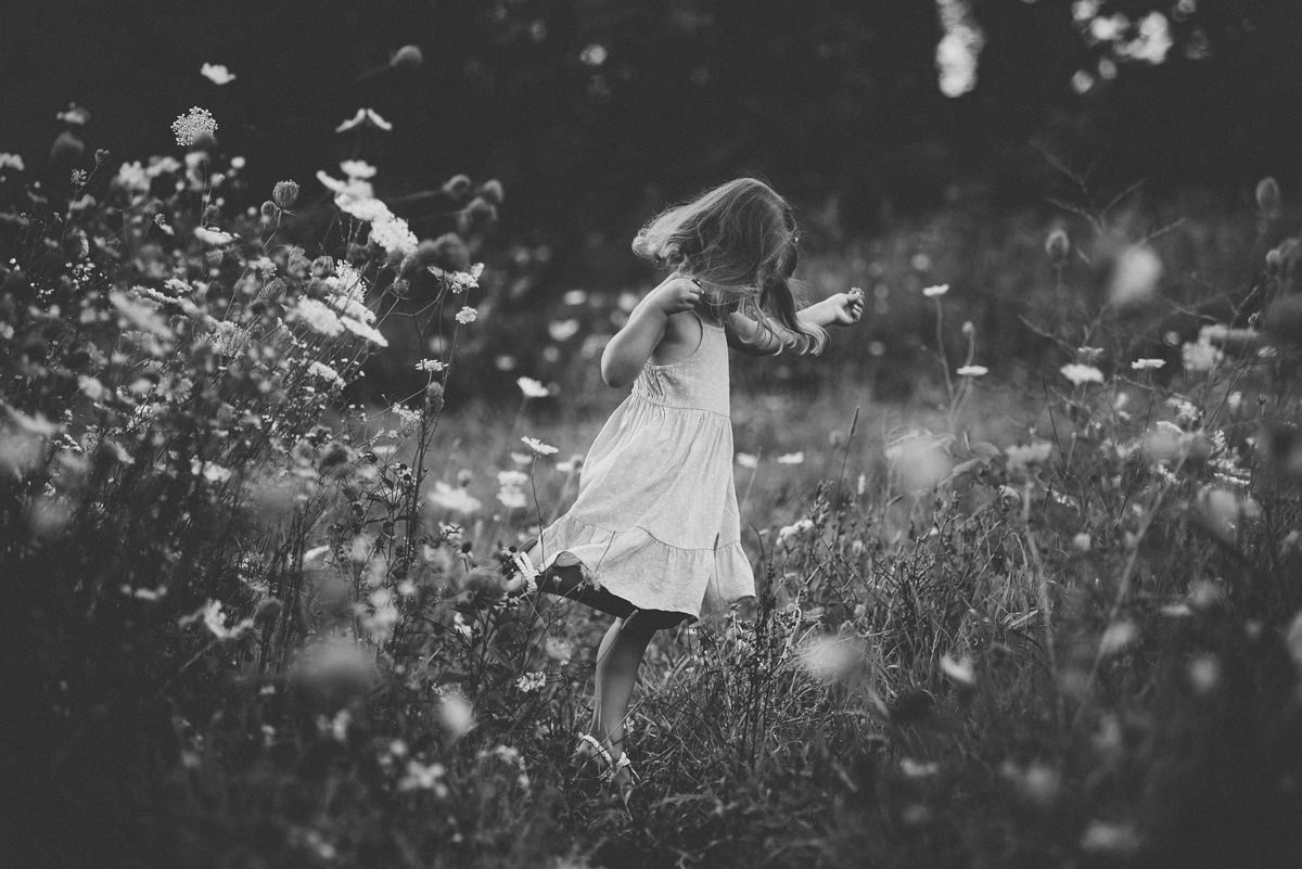 Black and white image of a child twirling in a meadow surrounded by floating seeds.