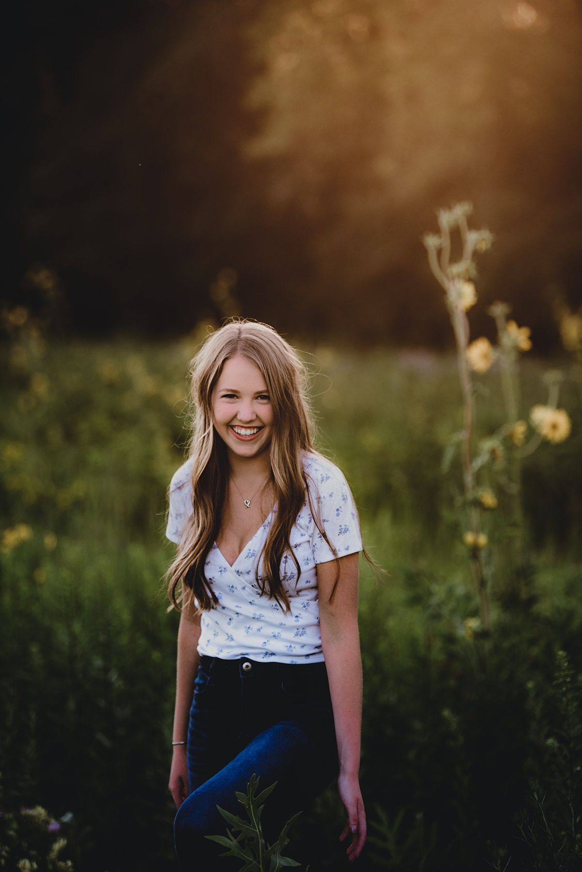 Outdoor portrait at sunset among yellow wildflowers with a white floral top.