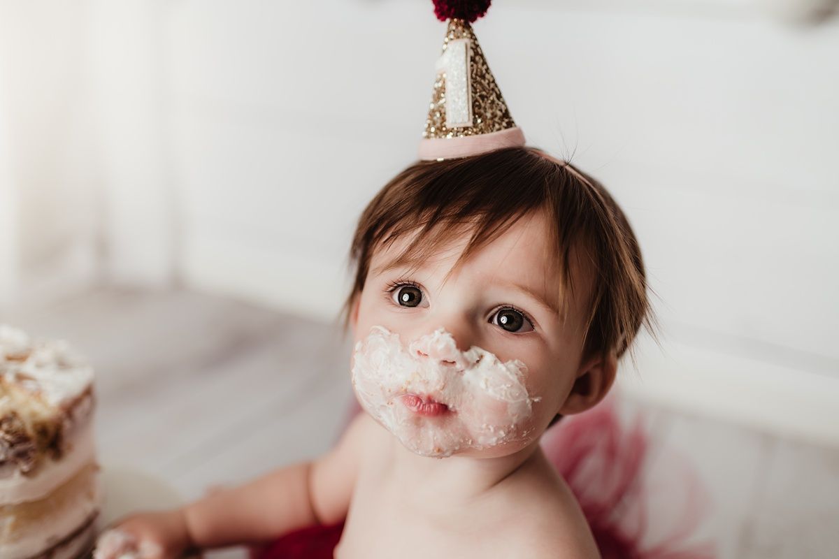 Close up of baby wearing party hat with cake frosting on face during cake smash photo shoot.