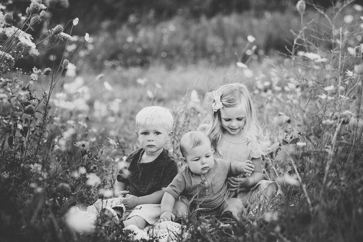 Black and white portrait of three children sitting among wildflowers.