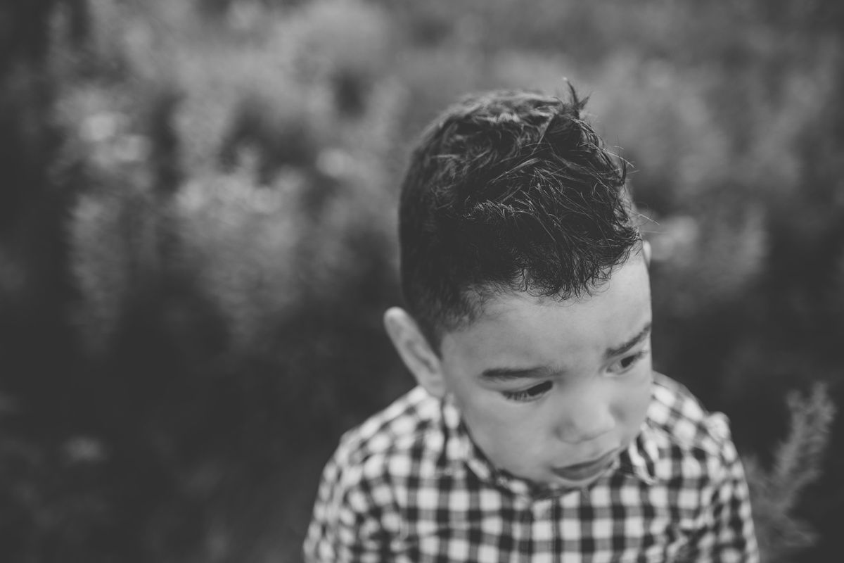 Black and white portrait of a child in gingham shirt looking downward thoughtfully.