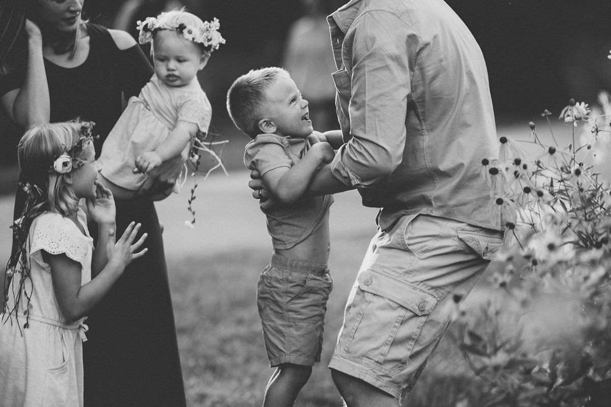 A candid black and white photo of a family sharing a playful moment outdoors.