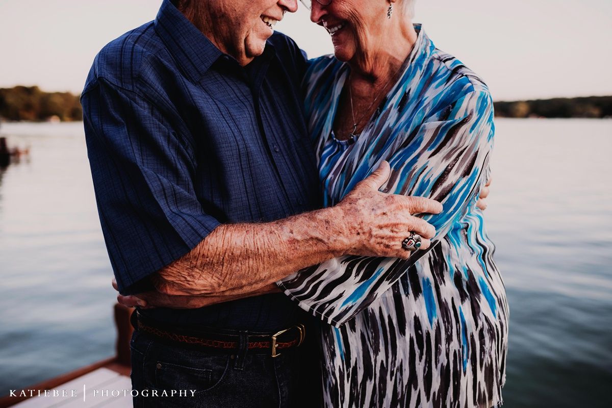 Senior couple embracing and laughing together by the water at sunset.
