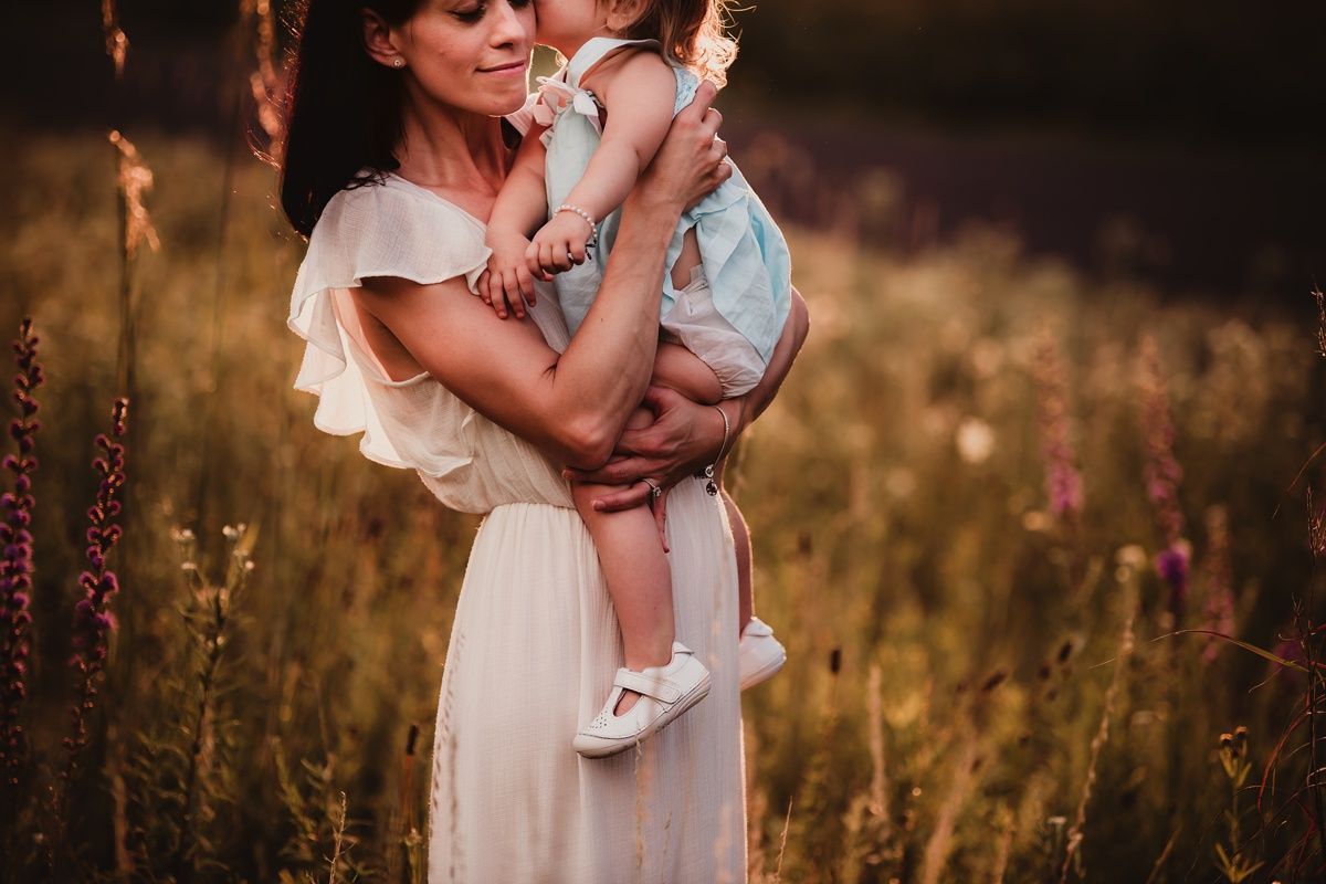 Parent and child share a loving moment in golden summer field at sunset.
