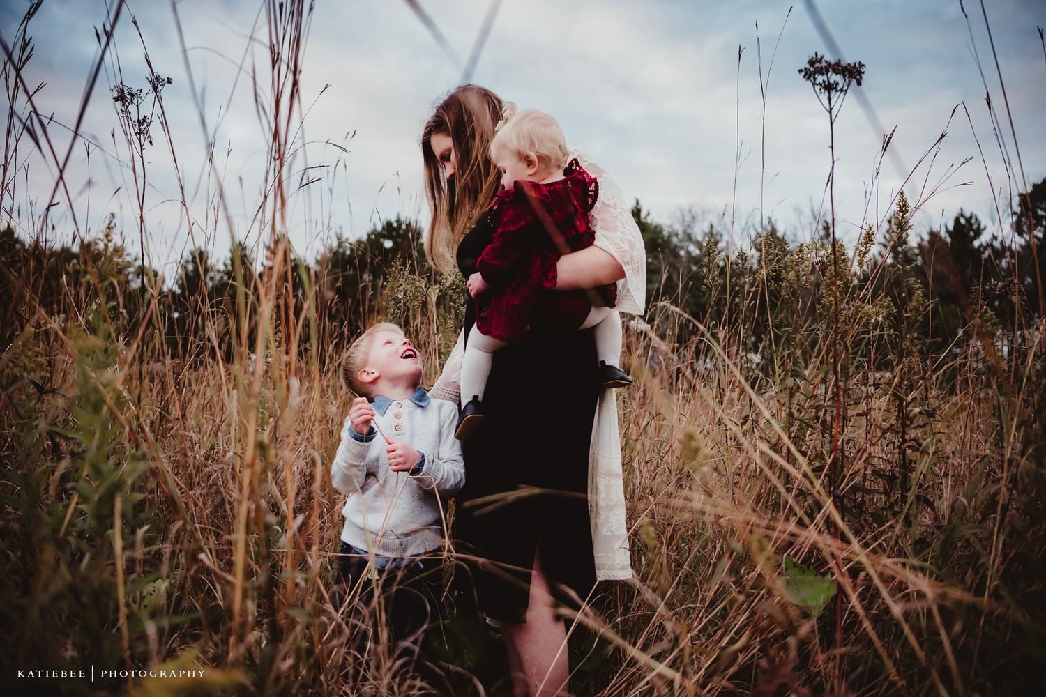 An intimate family moment captured in a field of tall autumn grass during golden hour.