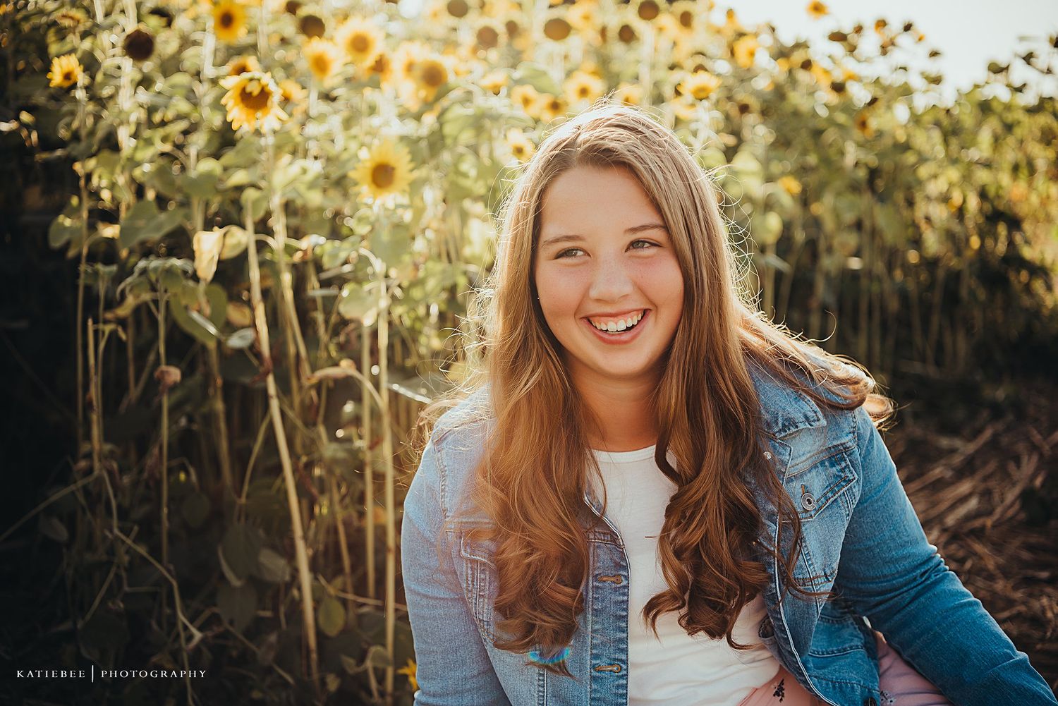 Candid portrait in a sunflower field wearing casual denim against golden evening light.