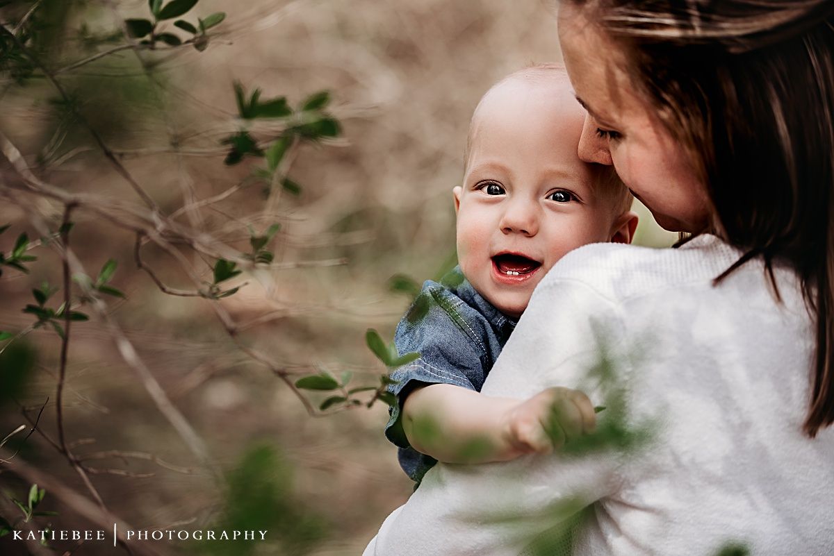 A sweet candid outdoor photo of loving parent and baby moment with greenery in background.