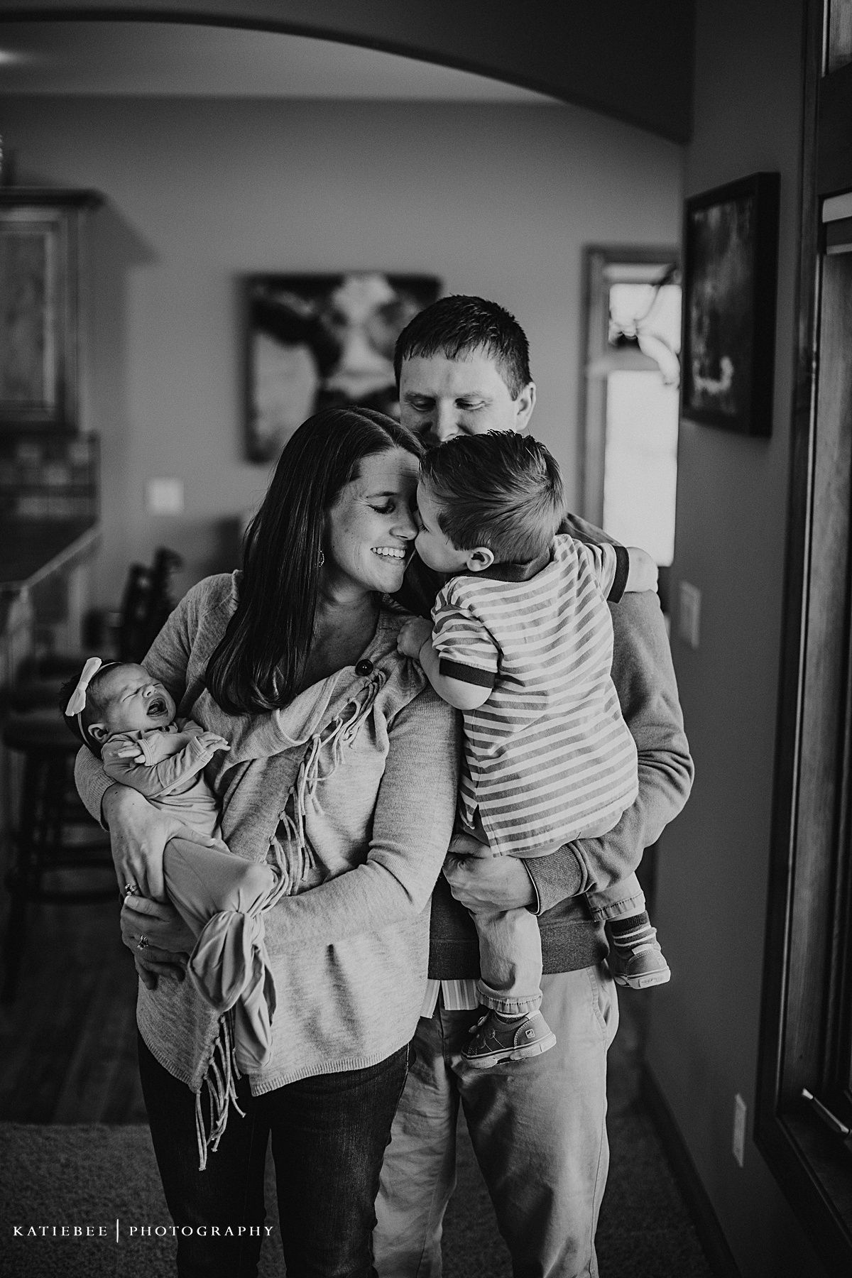 Black and white family portrait showing tender moment of embrace in home setting.