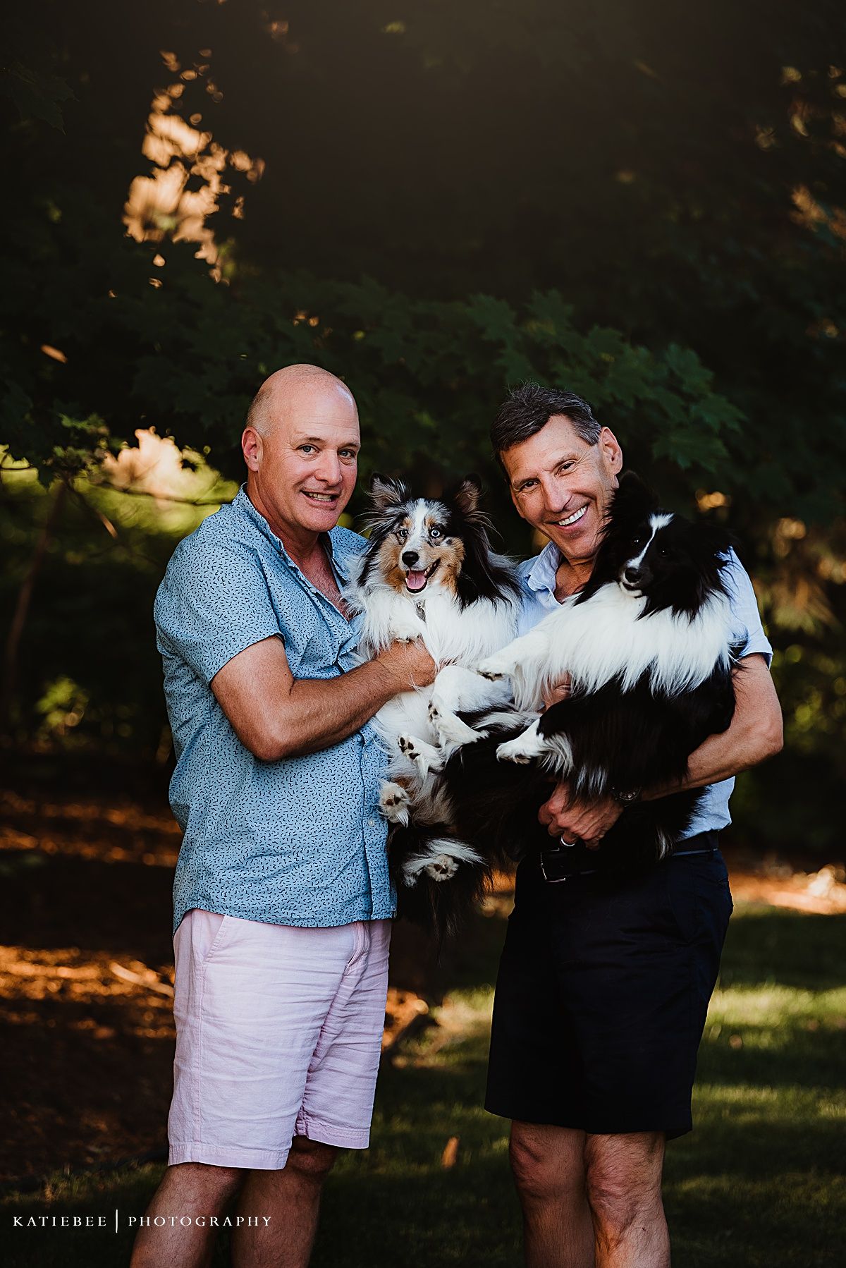 Two people in casual attire holding fluffy white dogs outdoors.