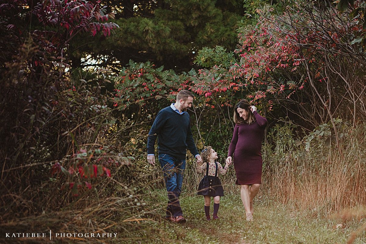 A family walks together on an autumn path lined with colorful foliage and trees.