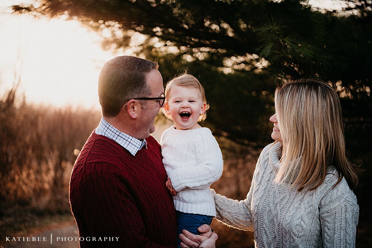 A warm family moment captured outdoors during golden hour with evergreen trees in the background.