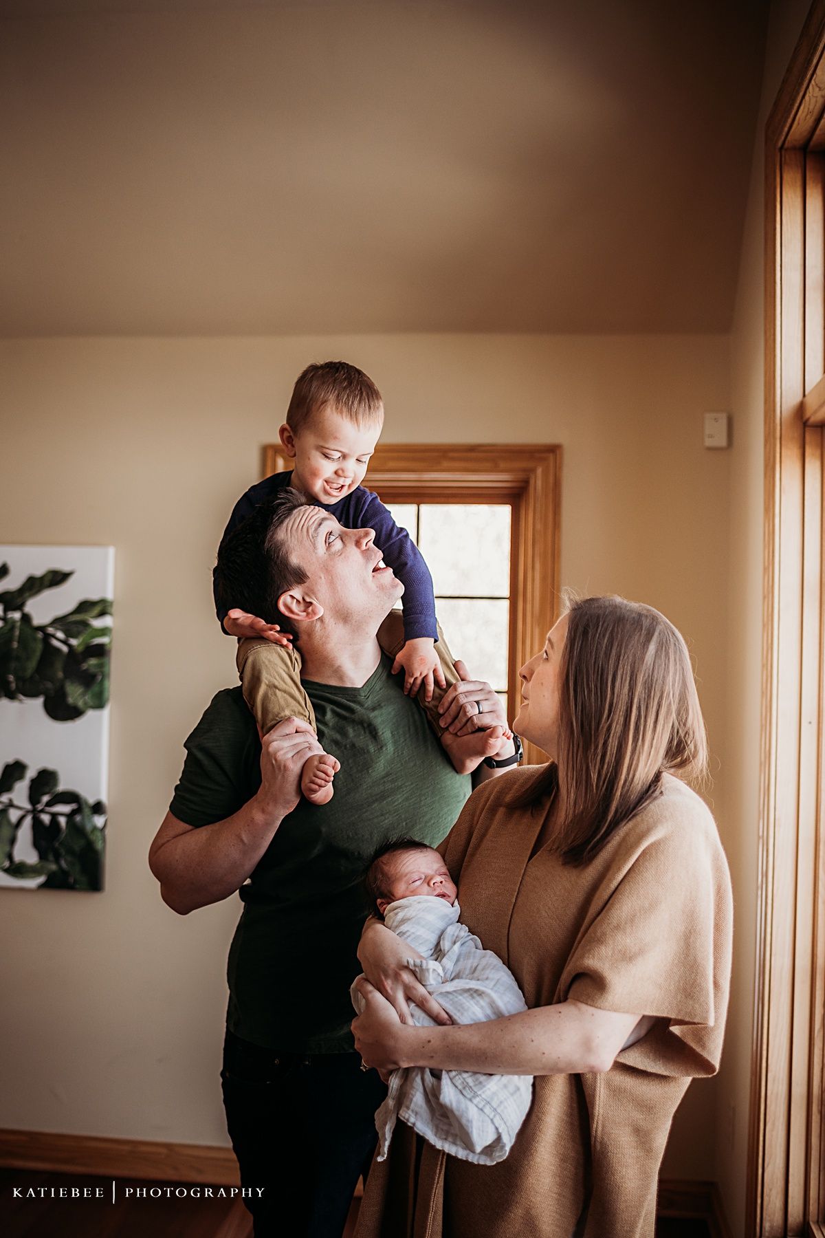 Joyful family moment with parents holding children by window in natural light.