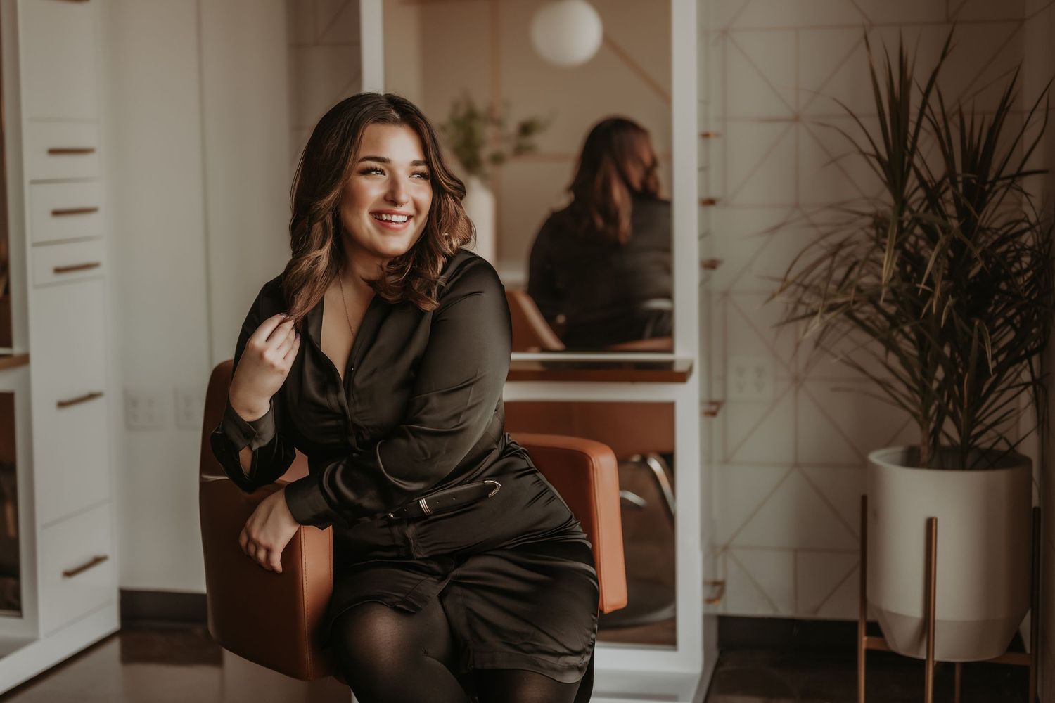 Professional portrait in modern salon setting with orange chair and minimalist decor.