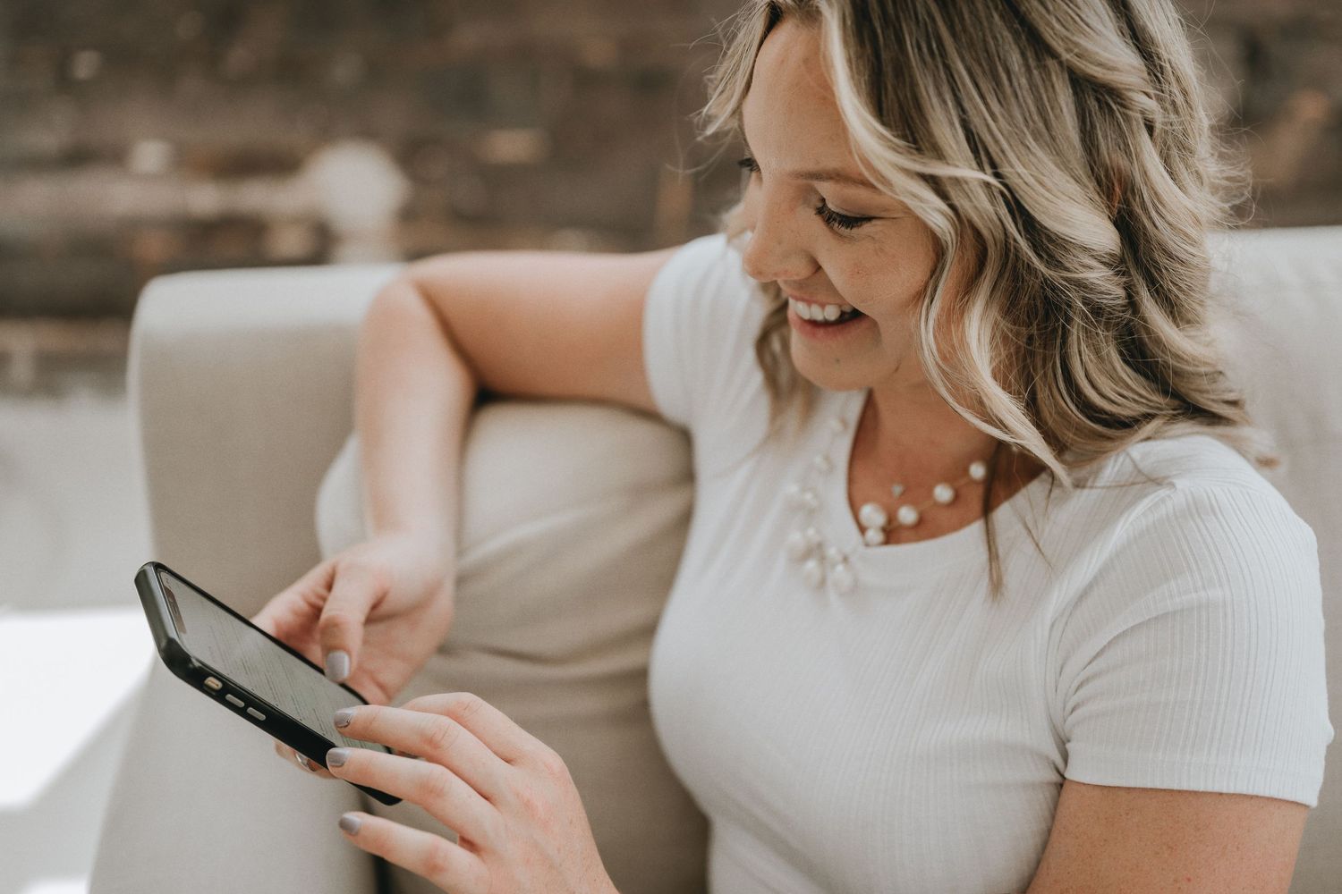 Woman in white t-shirt smiles while using digital tablet on comfortable couch.