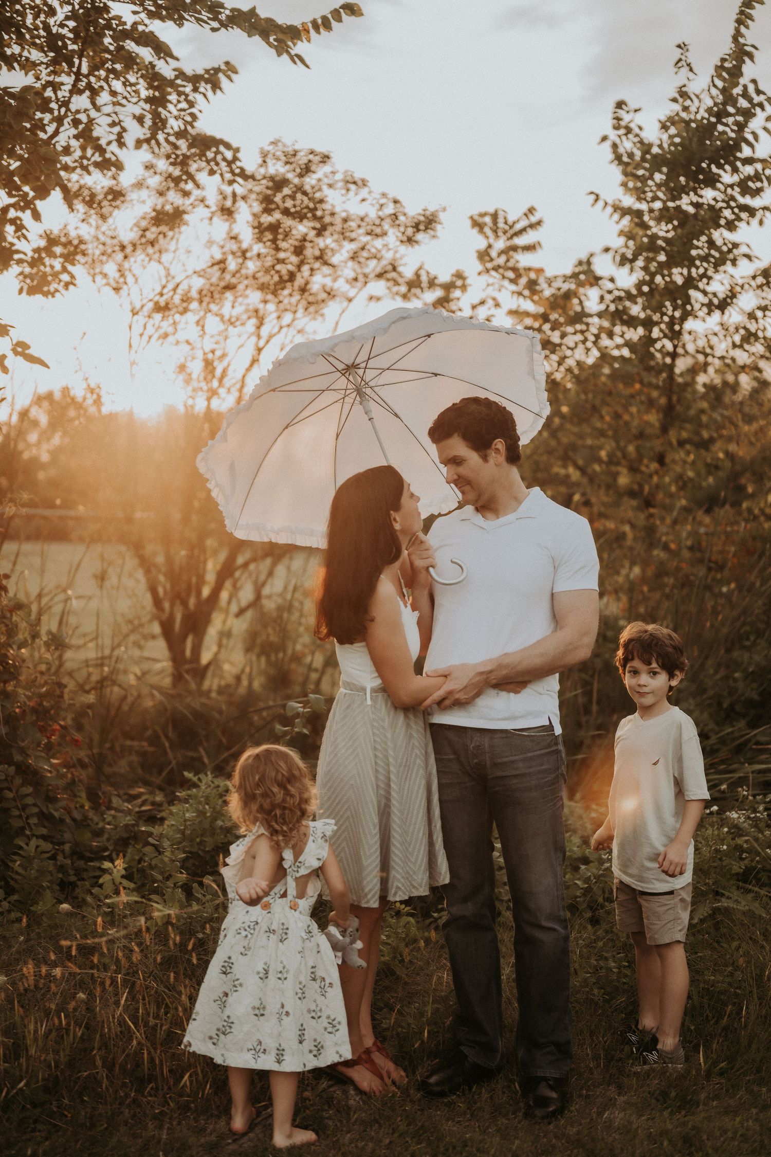 A family poses with a white umbrella in a field during sunset.