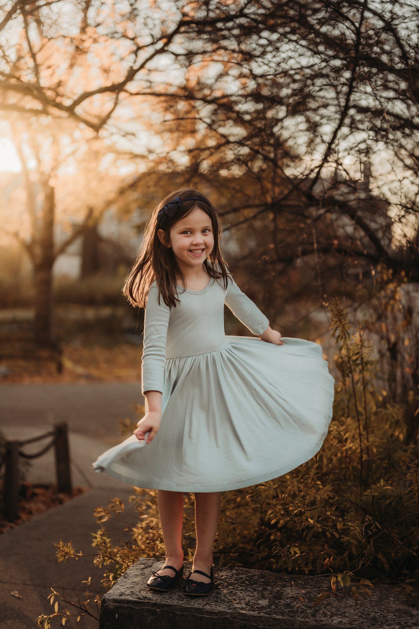 A light-colored dress twirls against an autumn sunset backdrop on a park path.