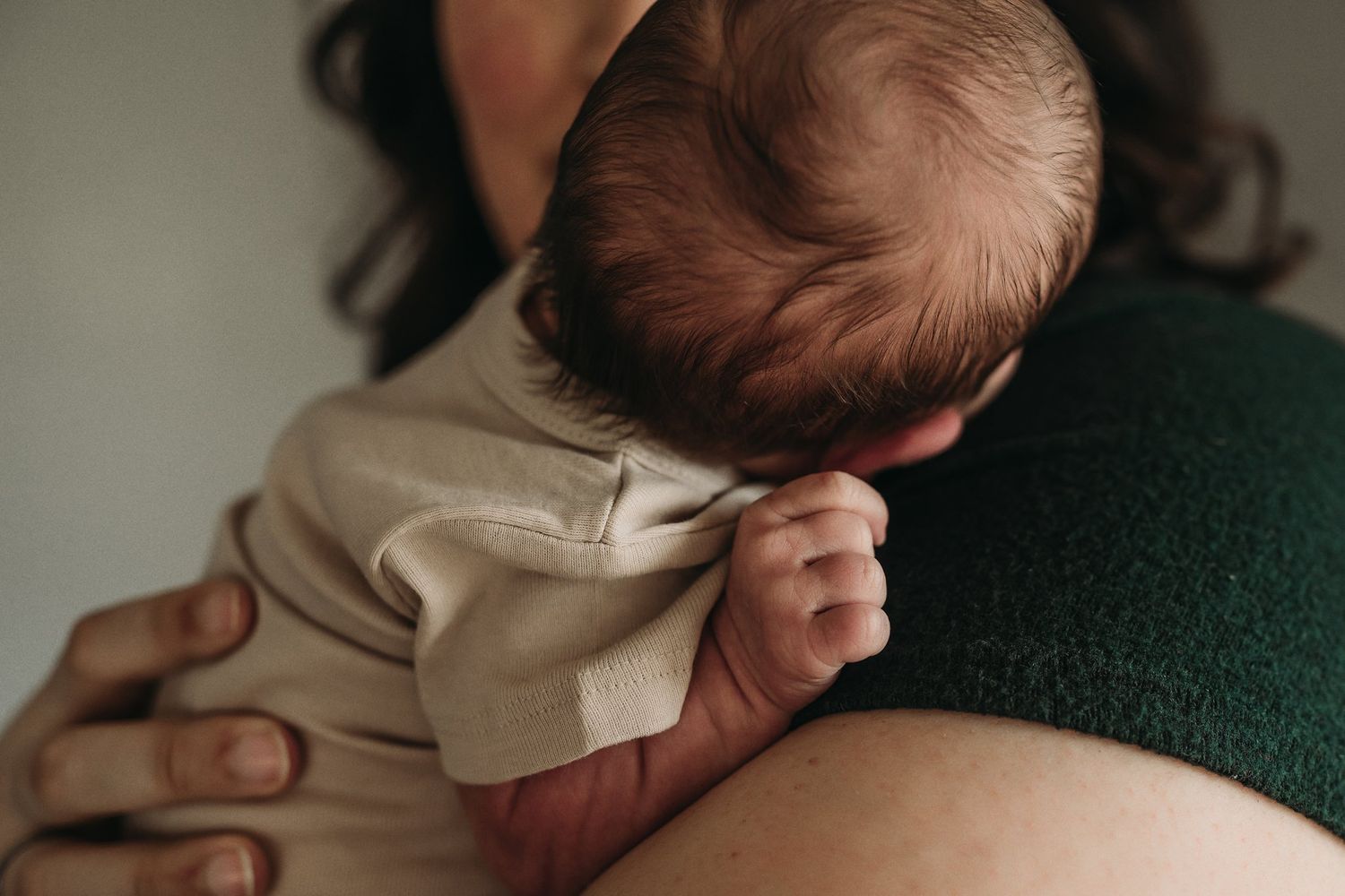 Newborn baby in beige clothing resting against a green surface.