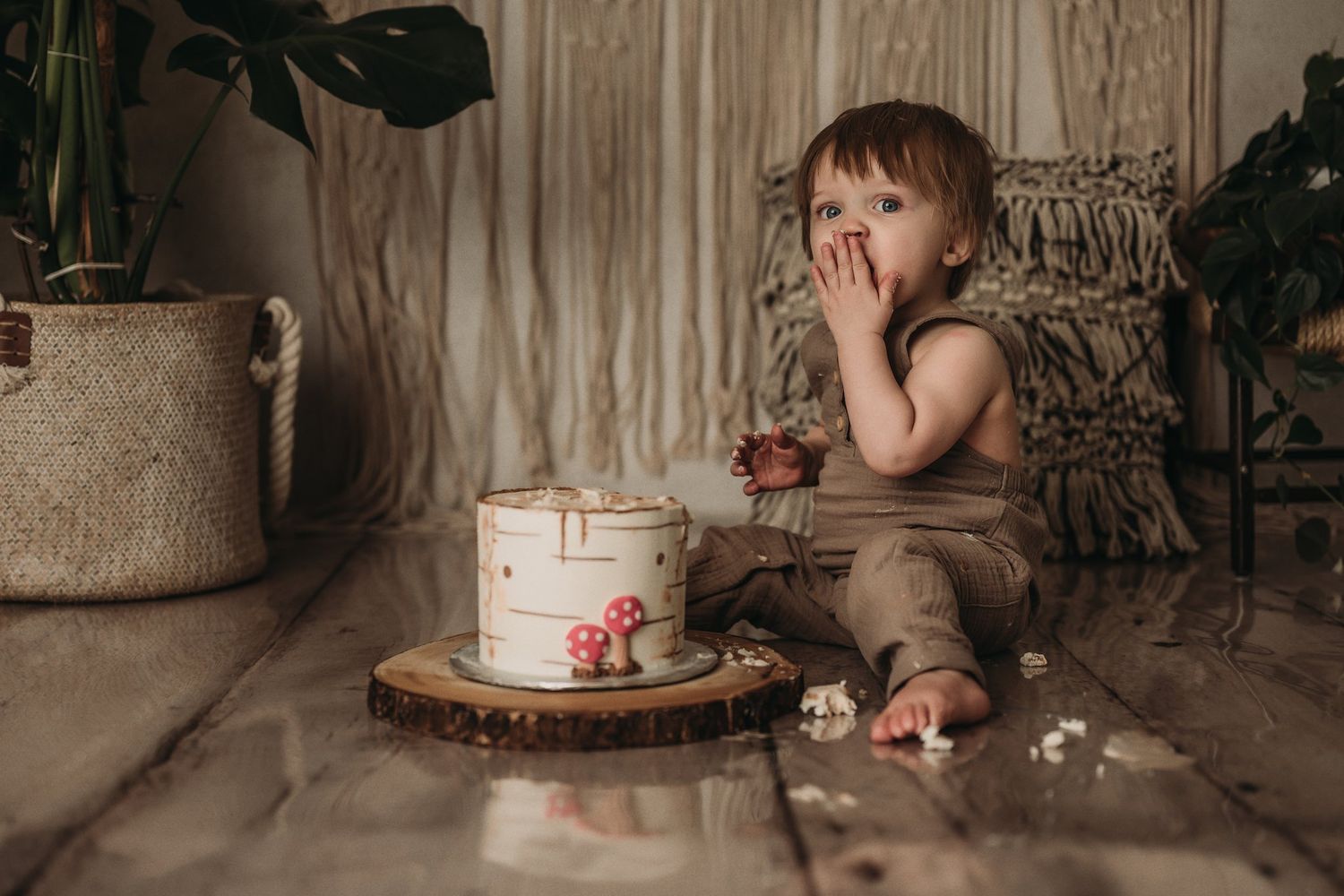 A woodland-themed birthday setup with a white birch cake on wooden slice and decorative macrame backdrop.