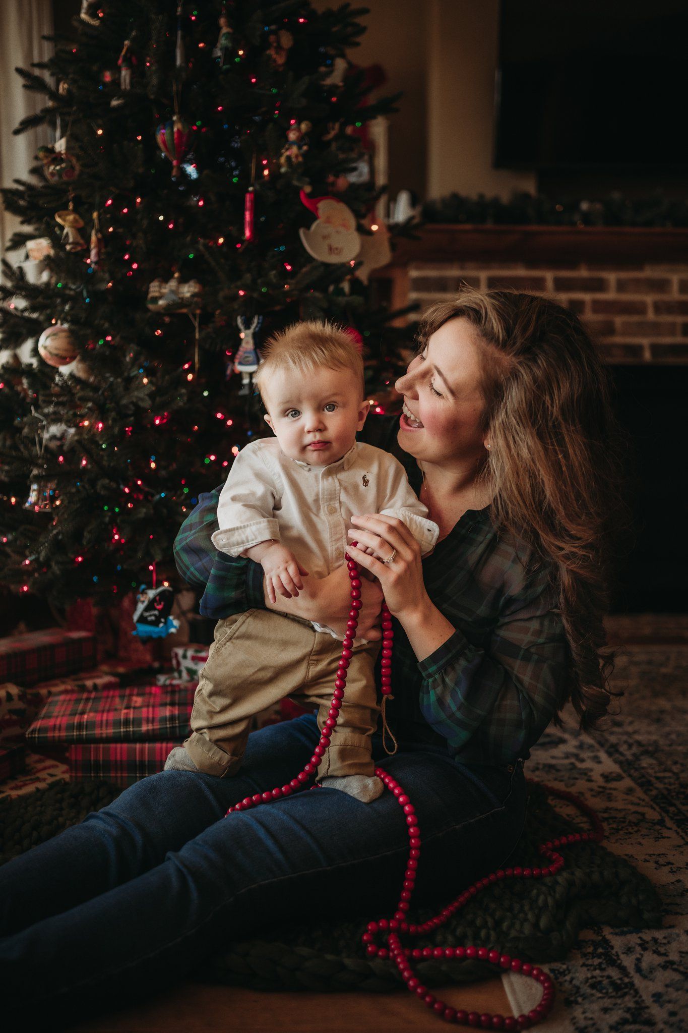 Intimate Christmas portrait with red beads and twinkling tree lights in background.